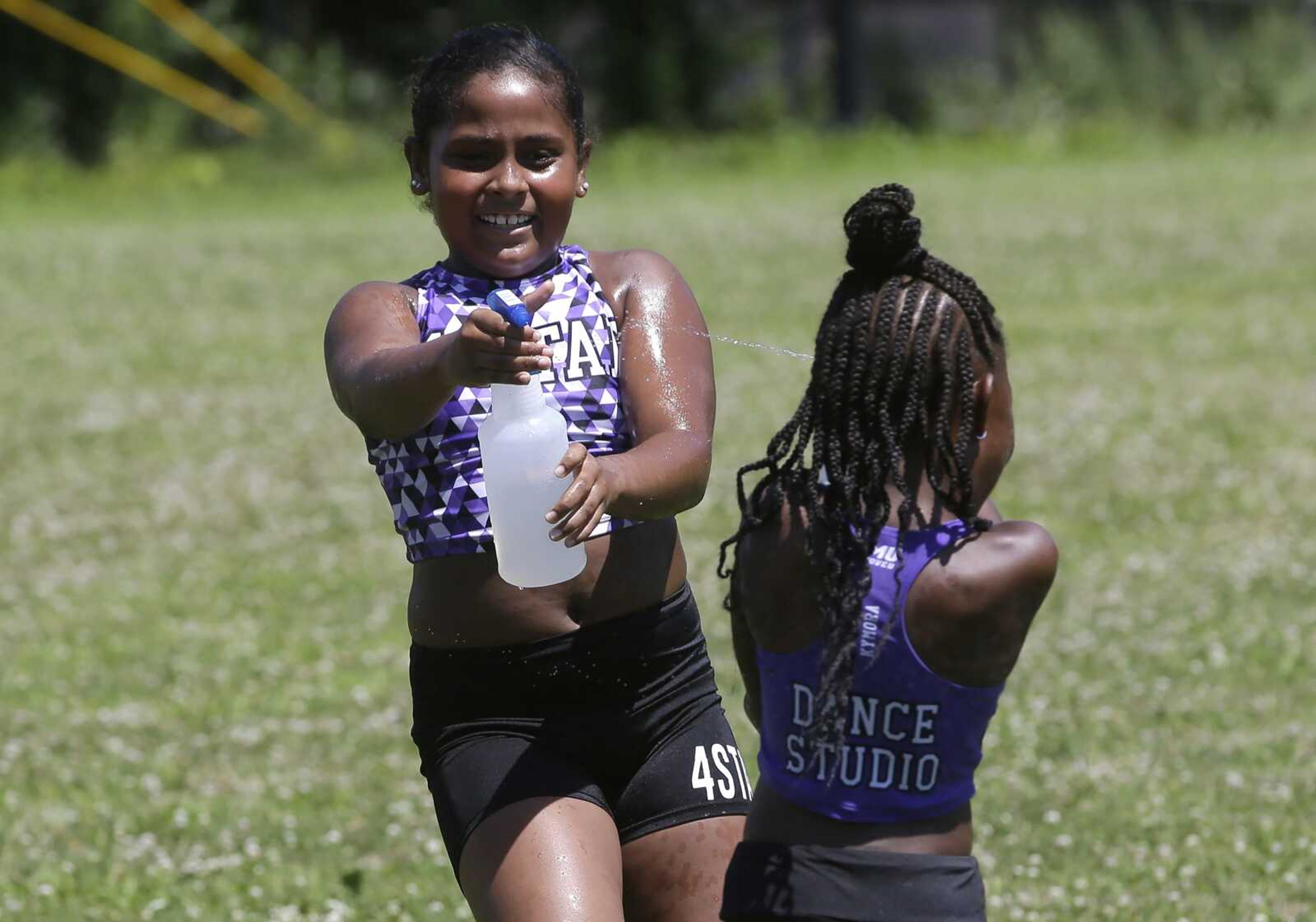 Dancers from the 4 Star Dance Studio Jazmyn Cawley-Zayas, 9, left, and Kymora McKoy-Johnson, 6, both of Boston, spray one another while cooling down after dancing in the Roxbury Unity Parade on Sunday in Boston's Roxbury neighborhood. Temperatures during the parade reached the 90s.