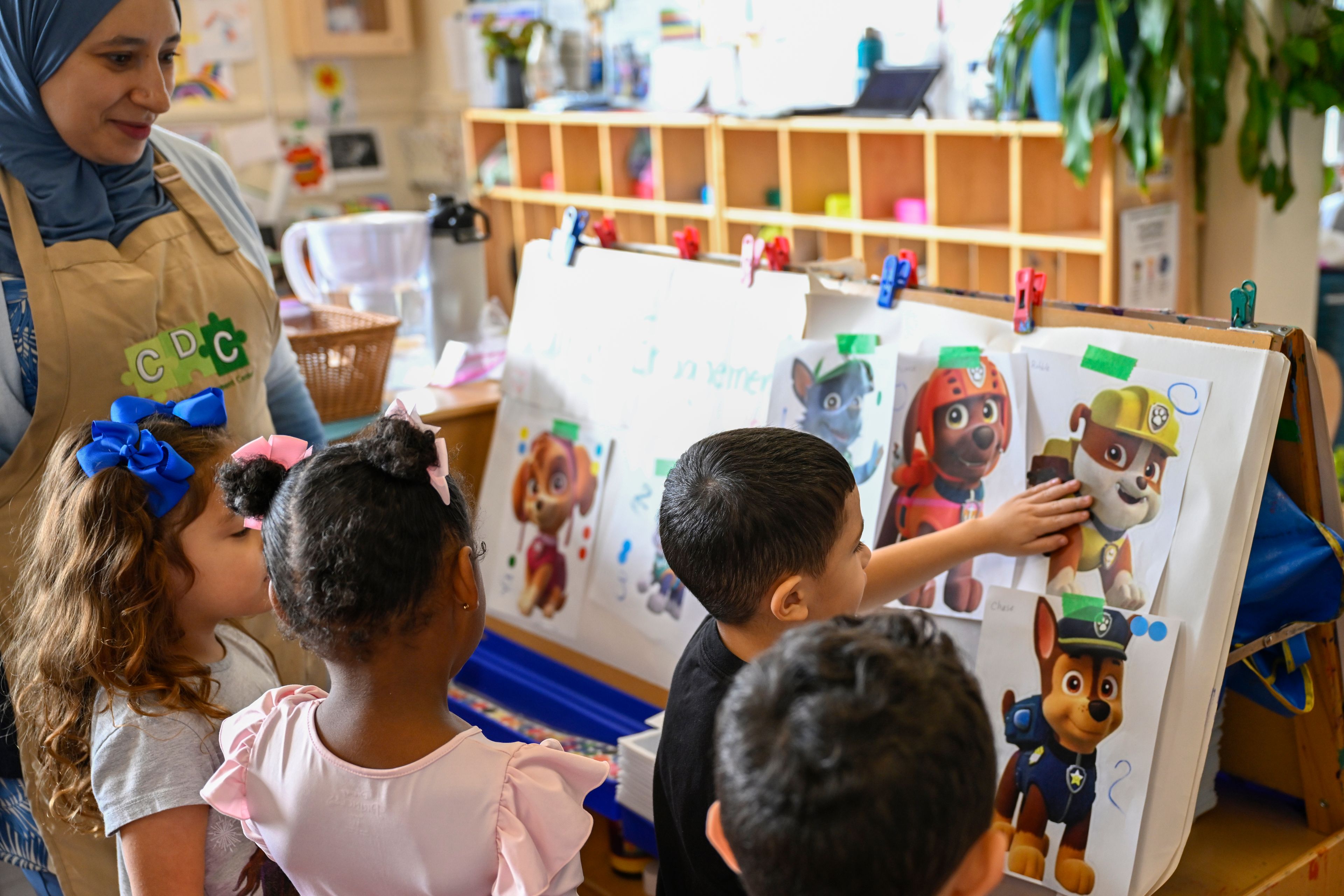 Preschool teacher Tinhinane Meziane, left, listens to her students on what characters of the TV show PAW Patrol they will vote for as their favorite character at the ACCA Child Development Center, Thursday, Sept. 19, 2024, in Annandale, Va. The students are getting foundational lessons on how to live in a democracy by allowing them to regularly vote on different things through out the day. (AP Photo/John McDonnell)