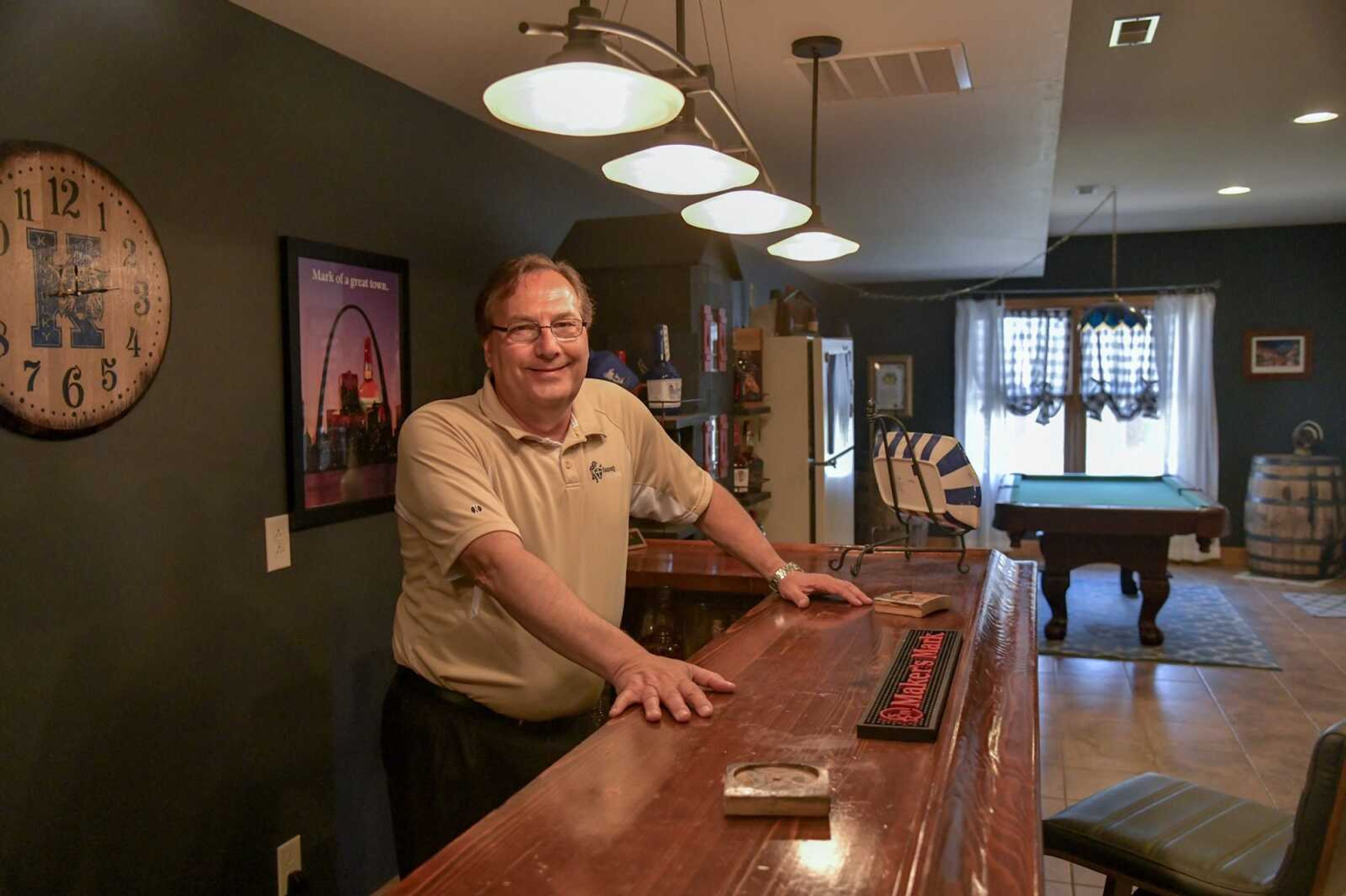 Mark Ruark poses for a photo at the bar in his man cave, behind him includes a collection of bourbon whiskey bottles and two barrels at his home in Cape Girardeau.