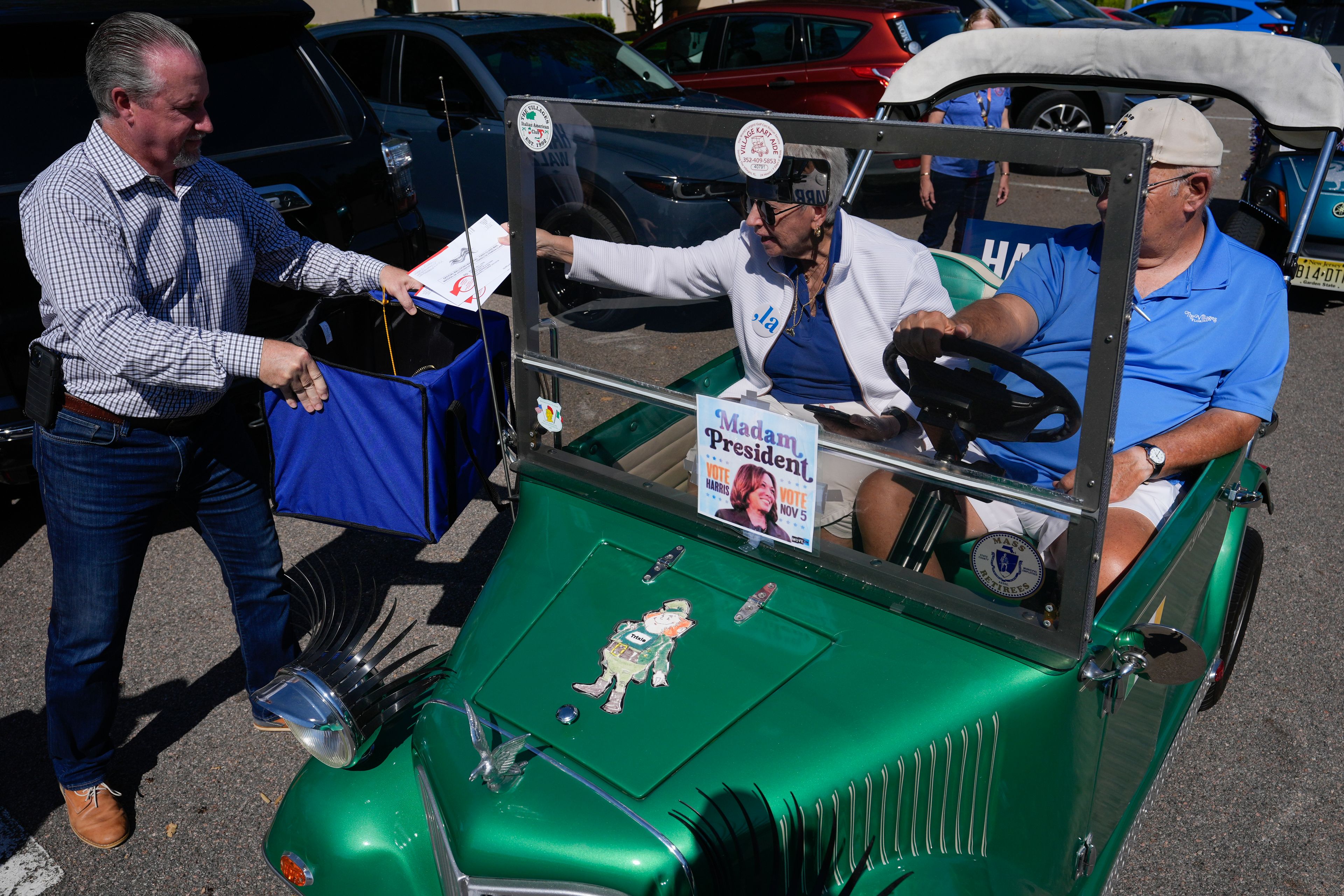 A couple drops their mail-in ballots into a collection box held by Sumter County Supervisor of Elections Bill Keen, during a golf cart parade to deliver mail-in votes organized by the Villages Democratic Club, in The Villages, Fla., Monday, Oct. 14, 2024. (AP Photo/Rebecca Blackwell)