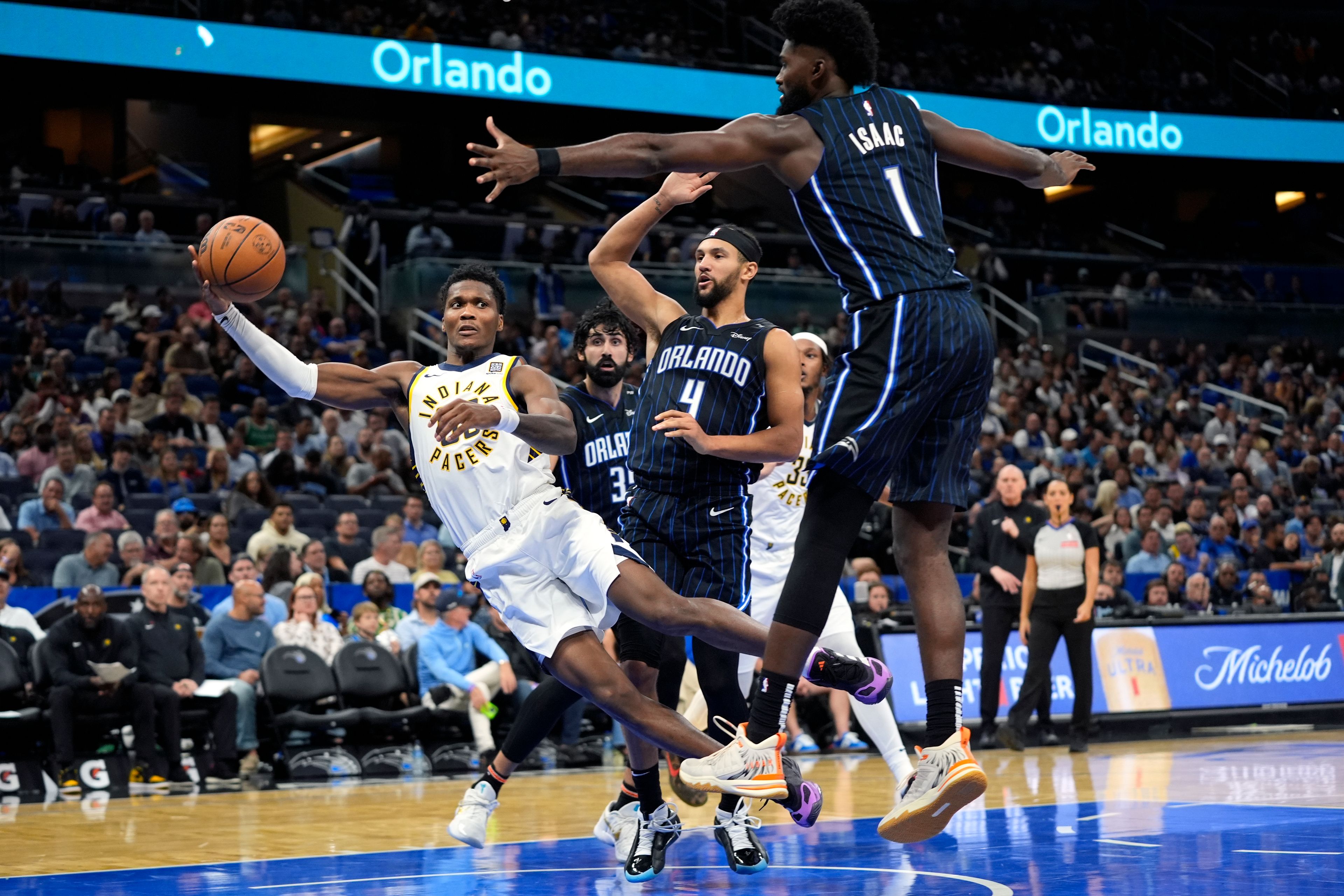 Indiana Pacers guard Bennedict Mathurin, center, dives between Orlando Magic guard Jalen Suggs (4) and forward Jonathan Isaac (1) to save the ball from going out of bounds during the second half of an NBA basketball game, Wednesday, Nov. 13, 2024, in Orlando, Fla. (AP Photo/John Raoux)