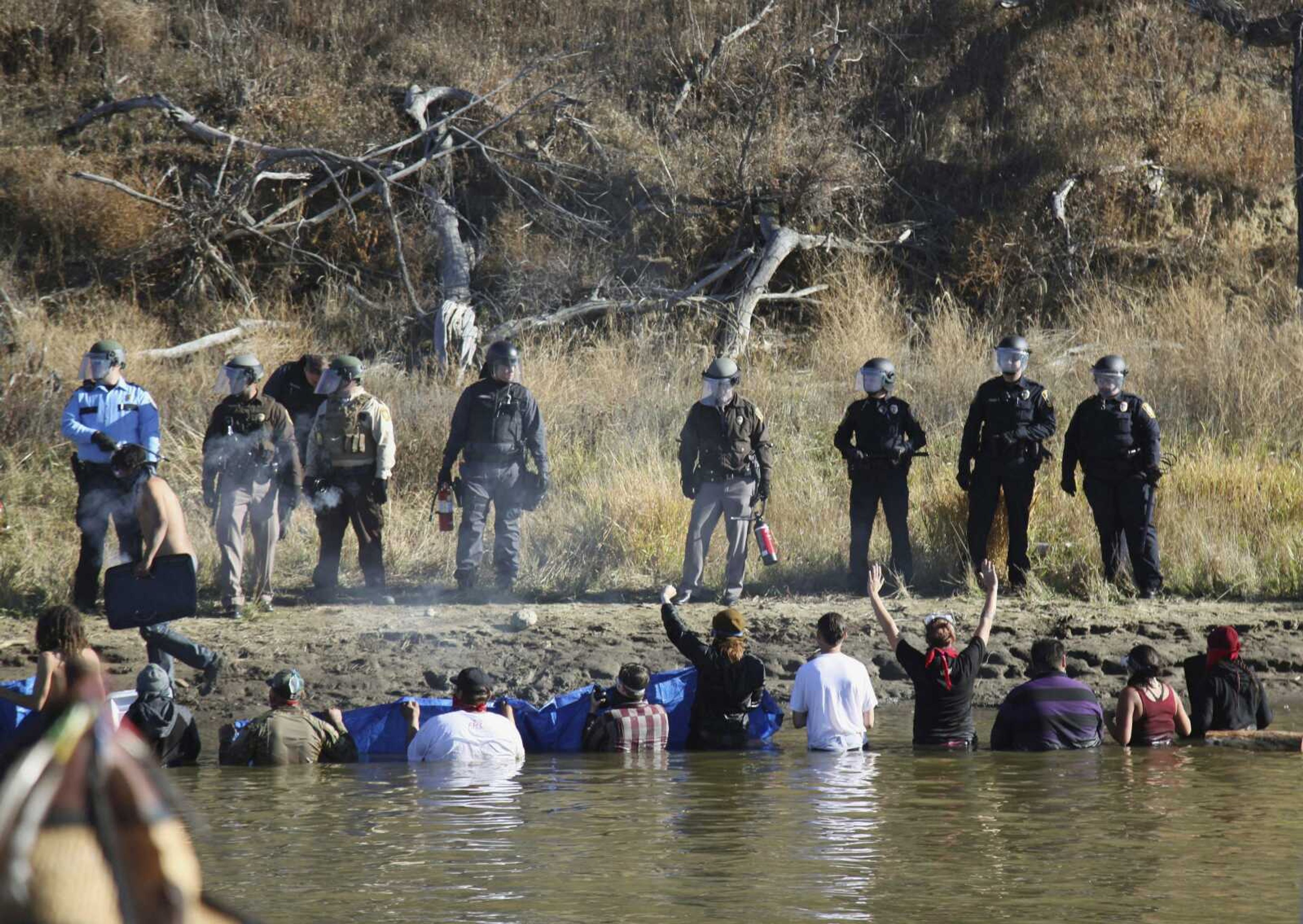 Protesters demonstrating against the expansion of the Dakota Access Pipeline wade in cold creek waters Nov. 2 to confront local police near Cannon Ball, North Dakota. The cost of policing the Dakota Access pipeline protests in North Dakota is at least $22 million -- more than $5 million more than the state set aside last year.