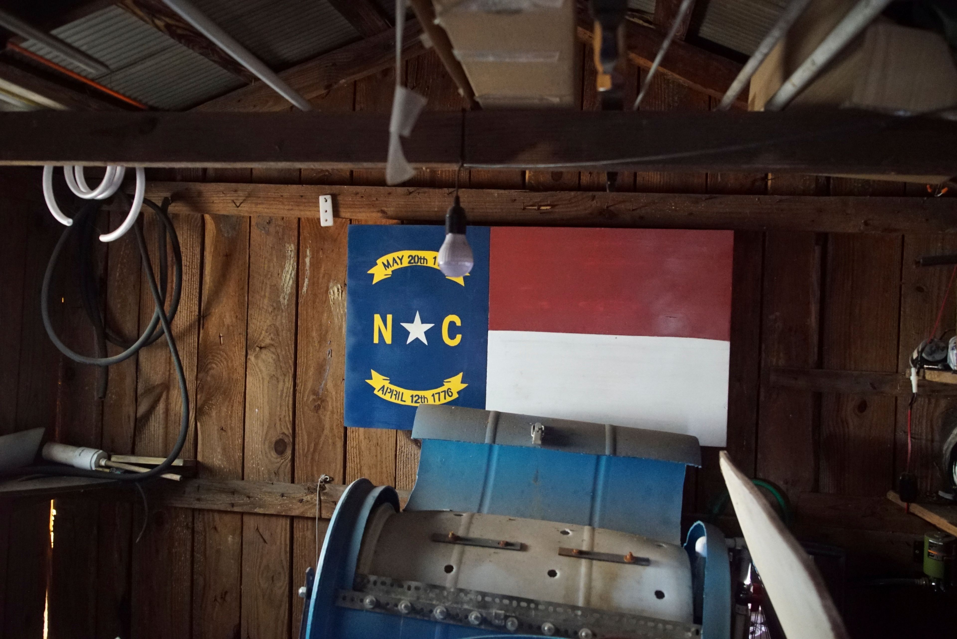 A wood panel painted with the North Carolina state flag hangs on the wall of a little barn behind Chris Arthur's home outside Mount Olive, N.C., on Monday, July 15, 2024. It was in this barn that the Army veteran spoke with a government informant, whose recording helped convict Arthur in federal court. (AP Photo/Allen G. Breed)