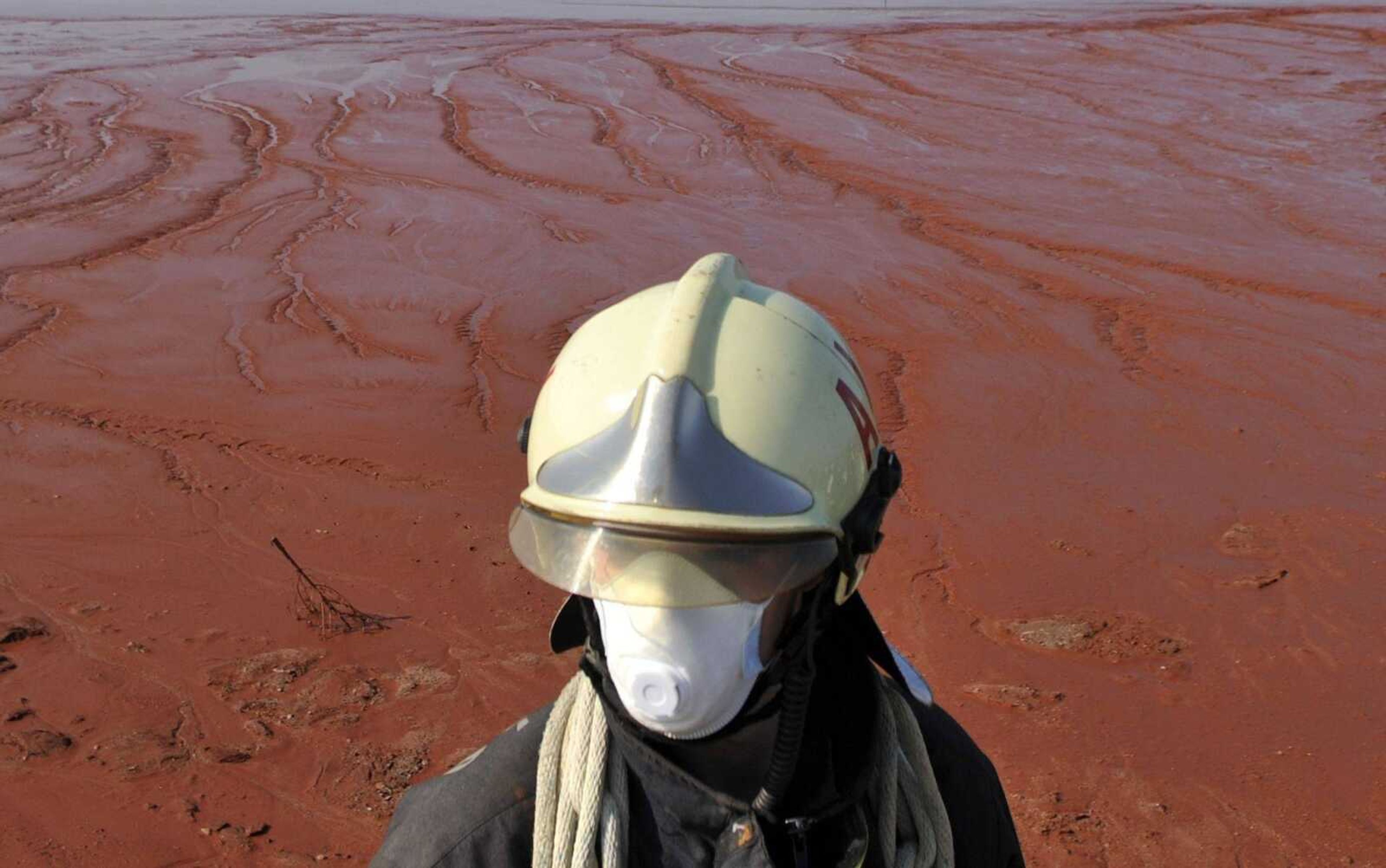 A Hungarian firefighter in protective gear stands guard Sunday at the red sludge reservoir, where a rupture caused deadly sludge flood in Kolontar, Hungary. (Bela Szandelszky ~ Associated Press)