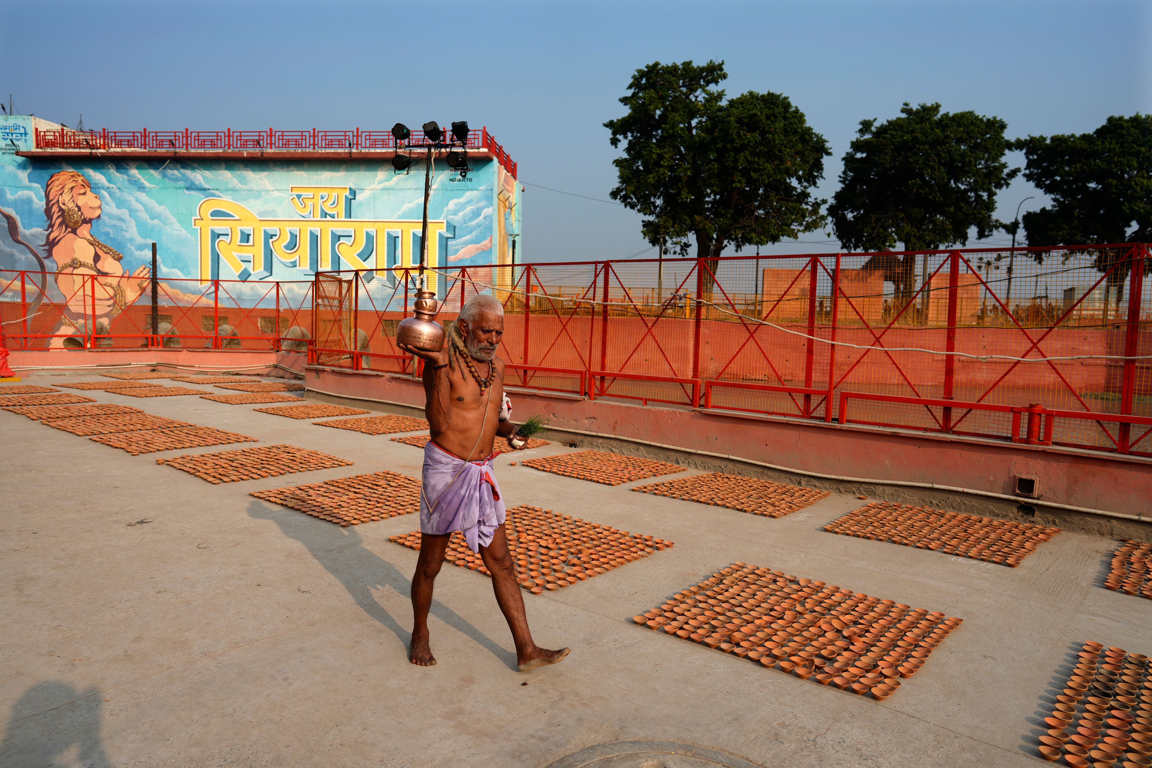 A Hindu holy man walks past earthen lamps in geometric patterns on the banks of the Saryu river on the morning of Deepotsav celebrations, an event organized by the Uttar Pradesh state government on the eve of Diwali, in Ayodhya, India, Wednesday, Oct. 30, 2024. (AP Photo/Rajesh Kumar Singh)