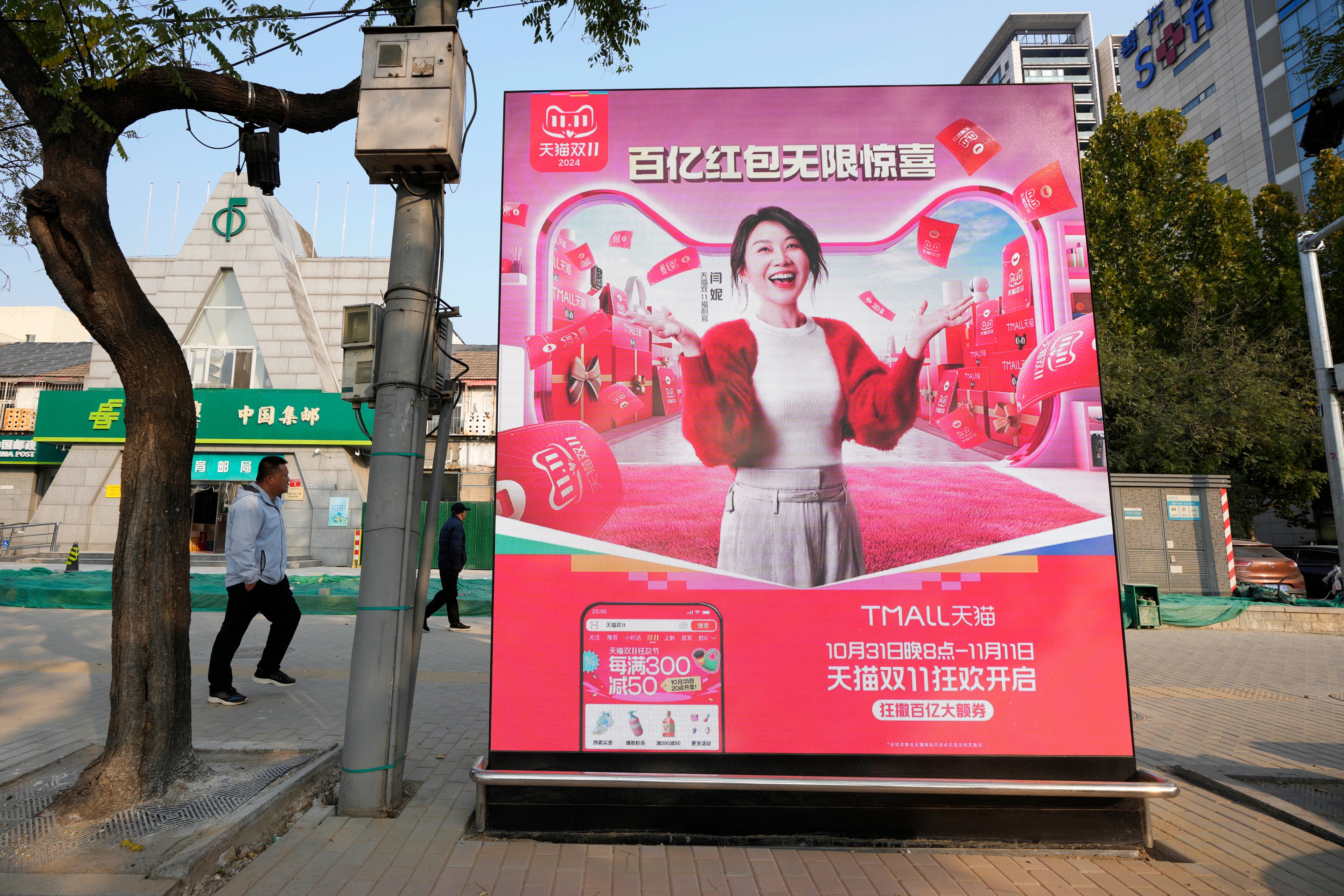 Pedestrians walk near an advertisement promoting a sales festival in Beijing, Thursday, Nov. 7, 2024. (AP Photo/Ng Han Guan)