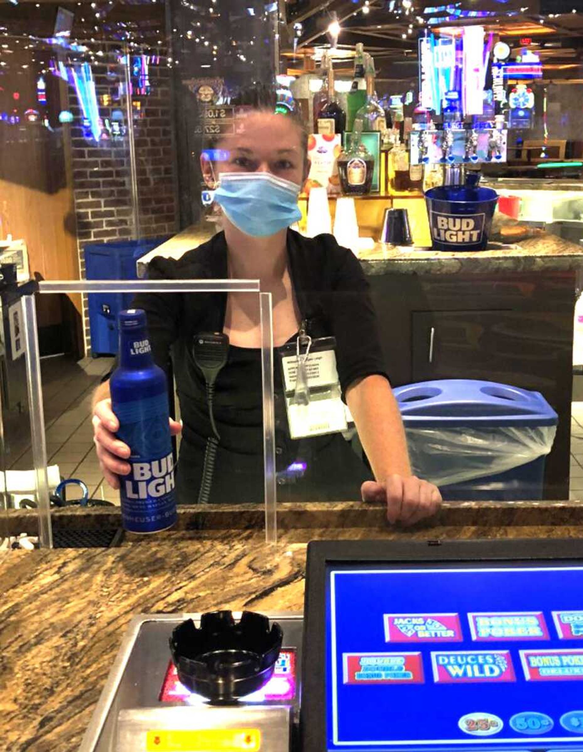 Morgan Williams serves a beverage through a opening in an acrylic barrier at the Century Casino Cape Girardeau video poker bar recently. Although she says the barrier can make it hard to hear customer orders, she appreciates the additional safety protection it provides for her and her customers.