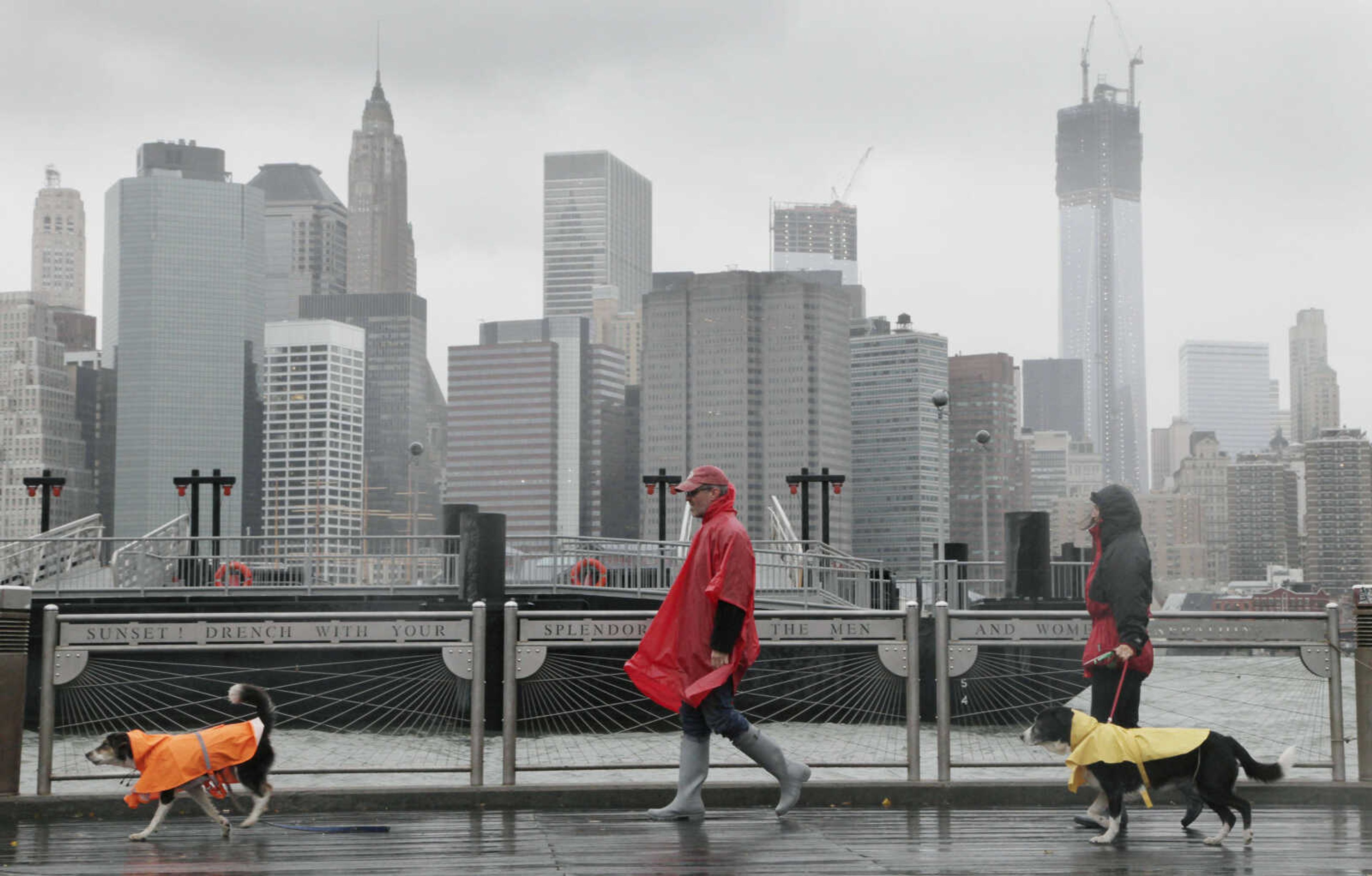 Peter Cusack, center, and Mel Bermudez walk their dogs Teague, left, and Molly along the Brooklyn waterfront beneath the New York skyline as Hurricane Sandy advances on the city, Monday, Oct. 29, 2012. Hurricane Sandy continued on its path Monday, forcing the shutdown of mass transit, schools and financial markets, sending coastal residents fleeing, and threatening a dangerous mix of high winds and soaking rain.Ę (AP Photo/Mark Lennihan)