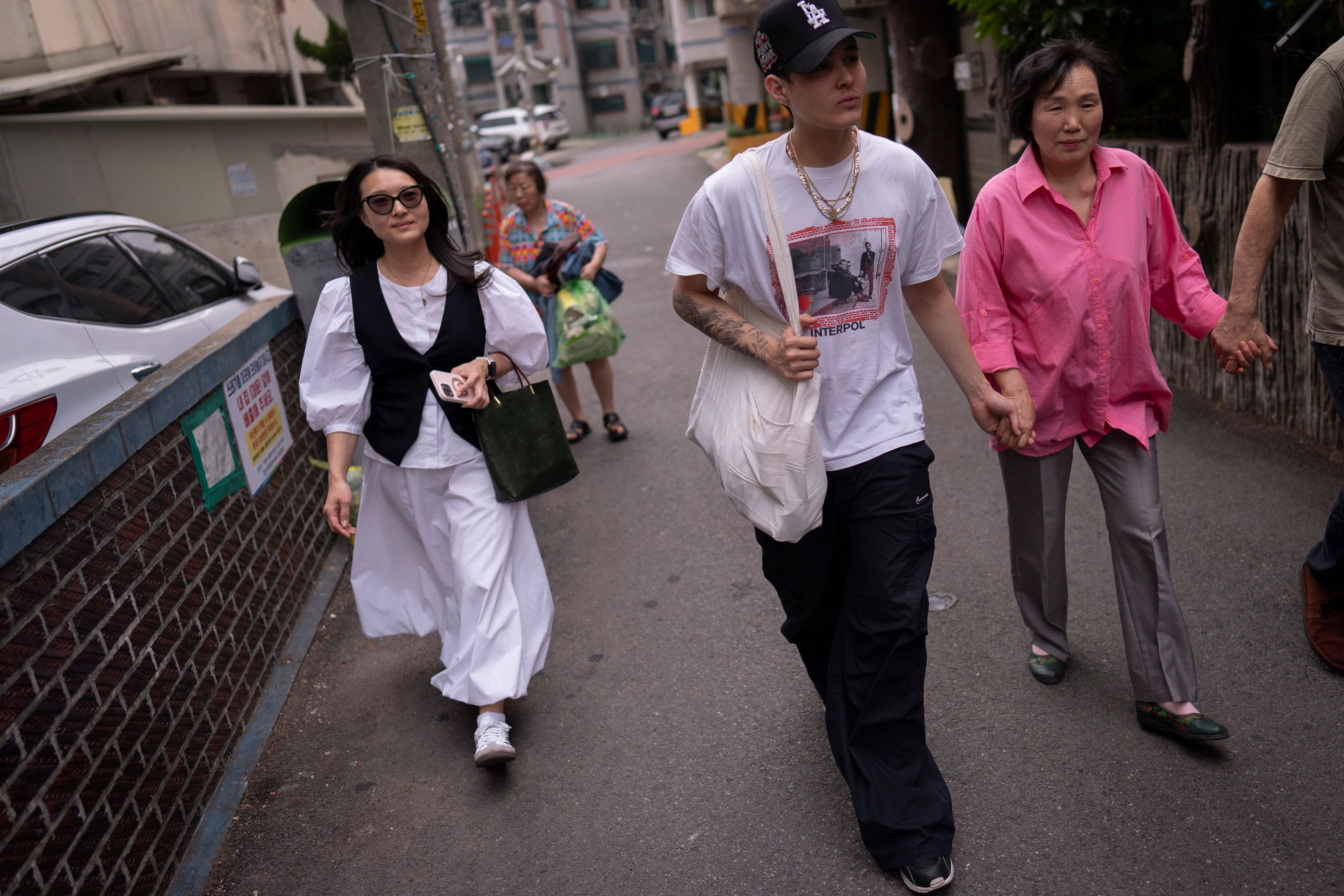 Nicole Motta, left, an adoptee visiting from Los Angeles to search for her birth family, visits the neighborhood where she was born in Bucheon, South Korea, Thursday, May 30, 2024. Her son, Adler, second from left, walks alongside long-time resident An Bok-rye who is helping with her search. (AP Photo/Jae C. Hong)