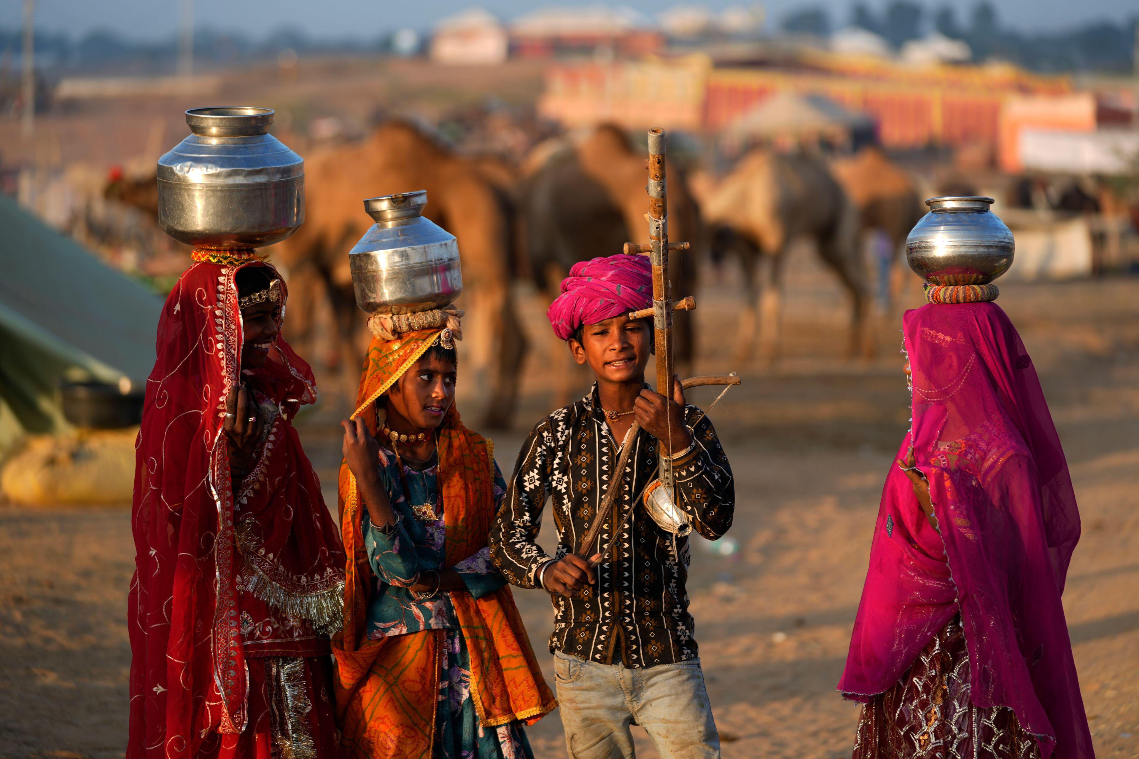 A child plays a string instrument as his companions carry water containers on their heads as they enact a scene from rural life during a camel fair in Pushkar, in the northwestern Indian state of Rajasthan, Wednesday, Nov. 13, 2024. (AP Photo/Deepak Sharma)