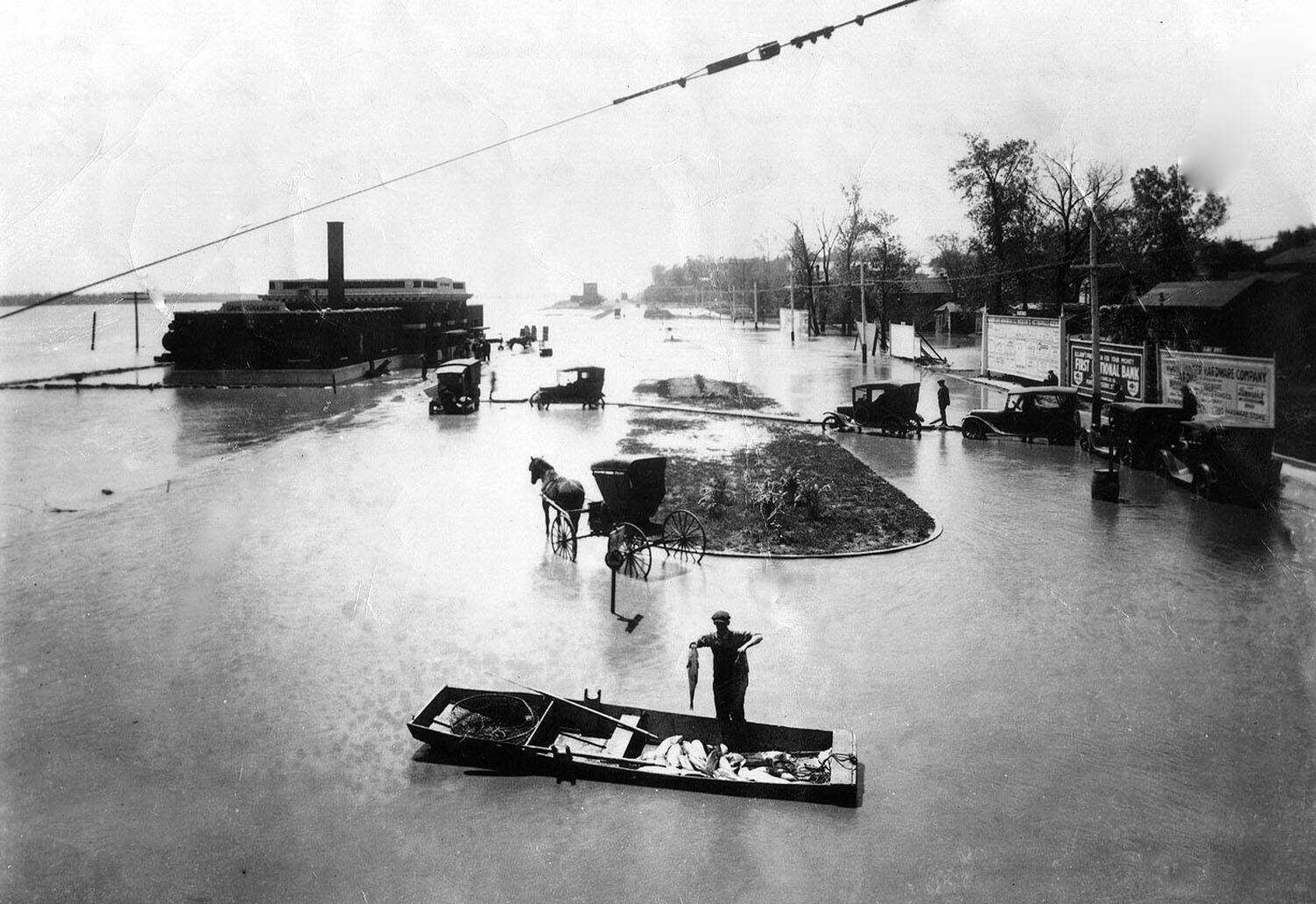 A fisherman shows off his catch in the lower part of this flood picture made at Main and Independence. Photo was likely taken between 1921 (when the Frisco depot was finished) and 1927 (when construction began on the traffic bridge). 