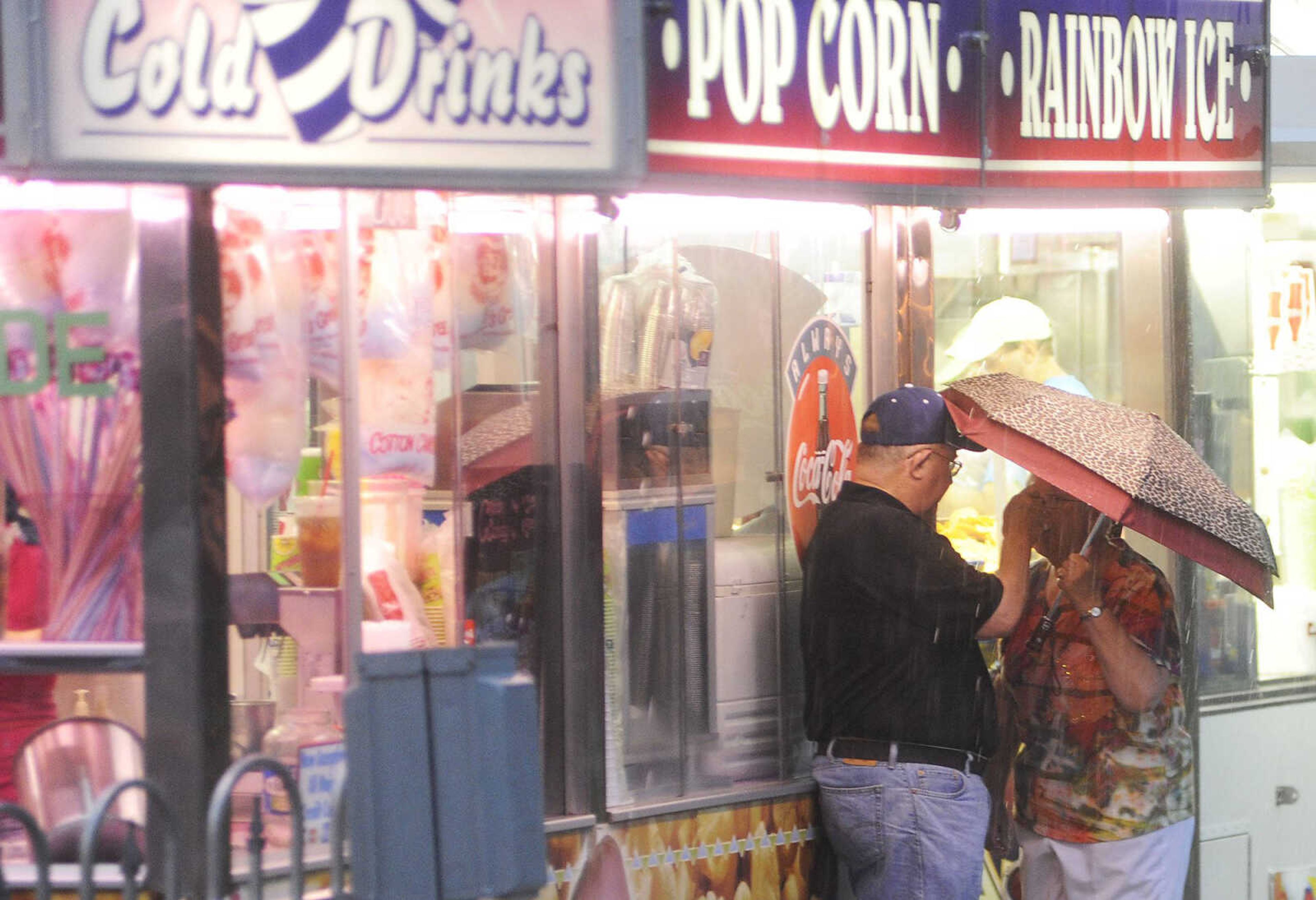 A couple share a snack while taking cover under an umbrella as a severe thunderstorm moves through Jackson causing outdoor performances to be canceled and the carnival to be shut down during the 105th Jackson Homecomers celebration Tuesday, July 23, in Jackson. (Adam Vogler)