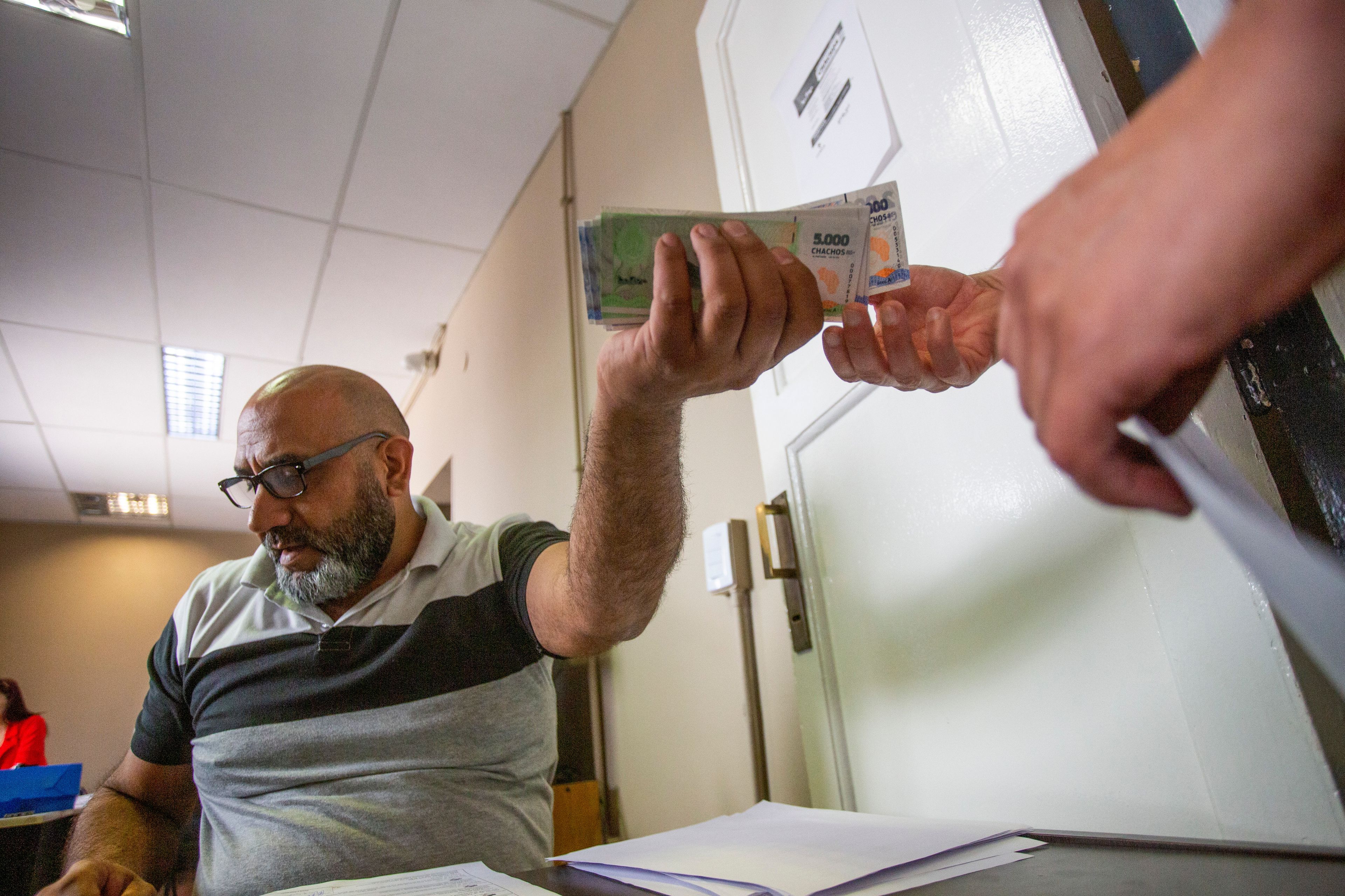 A state worker is paid with "chacho" currency in La Rioja, Argentina, Tuesday, Sept. 24, 2024. In response to slashed federal budgets to provinces, La Rioja is printing a new emergency tender called "chachos" to pay state workers and spur the economy. (AP Photo/Natalia Diaz)