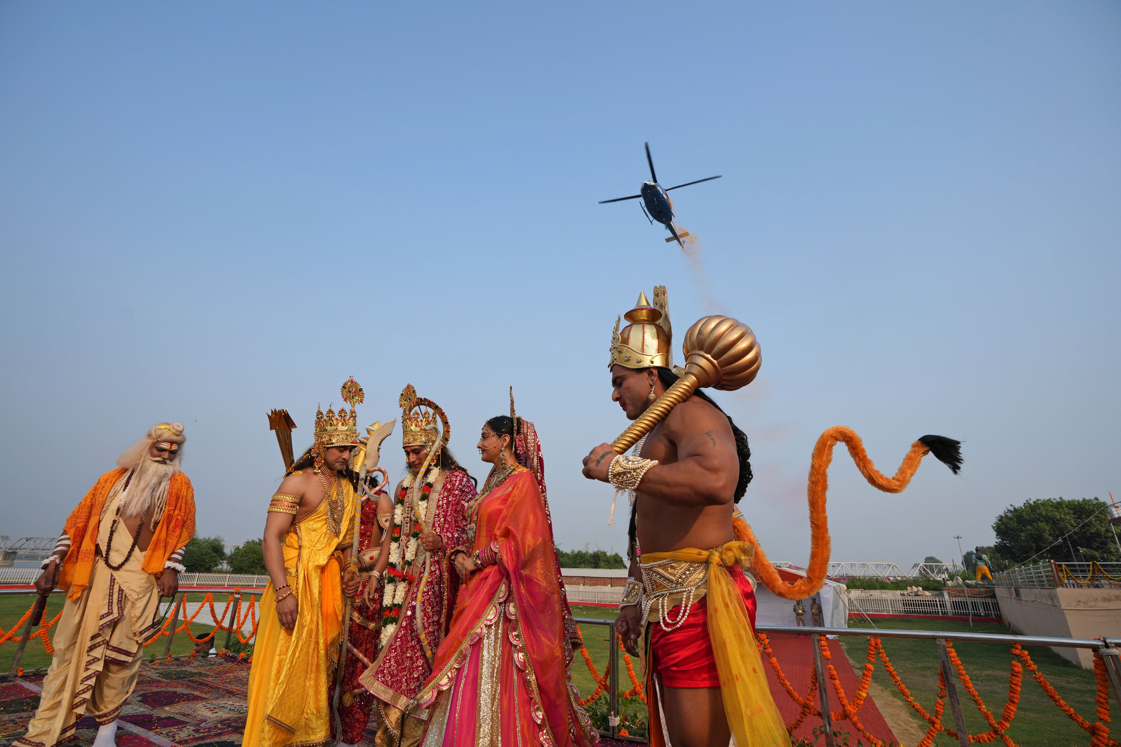 Actors playing Hindu god Rama, third left, and other deities stand as a helicopter showers flower petals during Deepotsav celebrations, an event organized by the Uttar Pradesh state government on the eve of Diwali, in Ayodhya, India, Wednesday, Oct. 30, 2024. (AP Photo/Rajesh Kumar Singh)