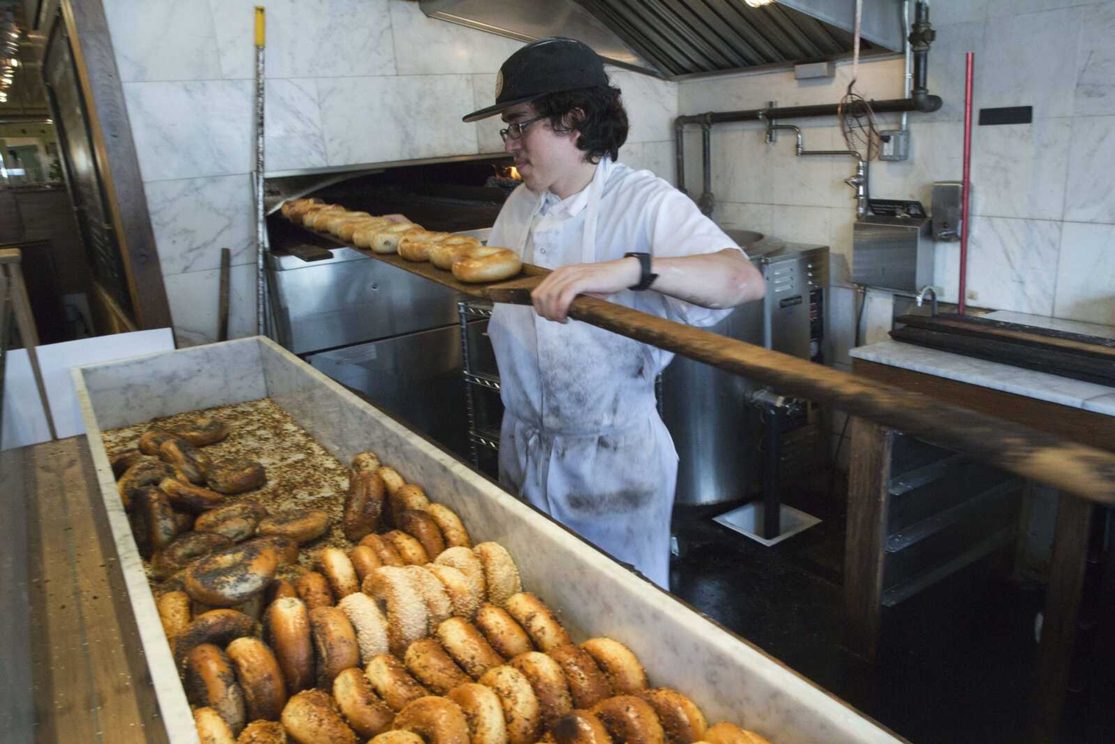 In this Friday, May 27, photo, baker Jefferson Arcila removes freshly baked bagels from the wood burning oven at the Black Seed bagel shop in the East Village neighborhood of New York. (AP Photo/Mary Altaffer)