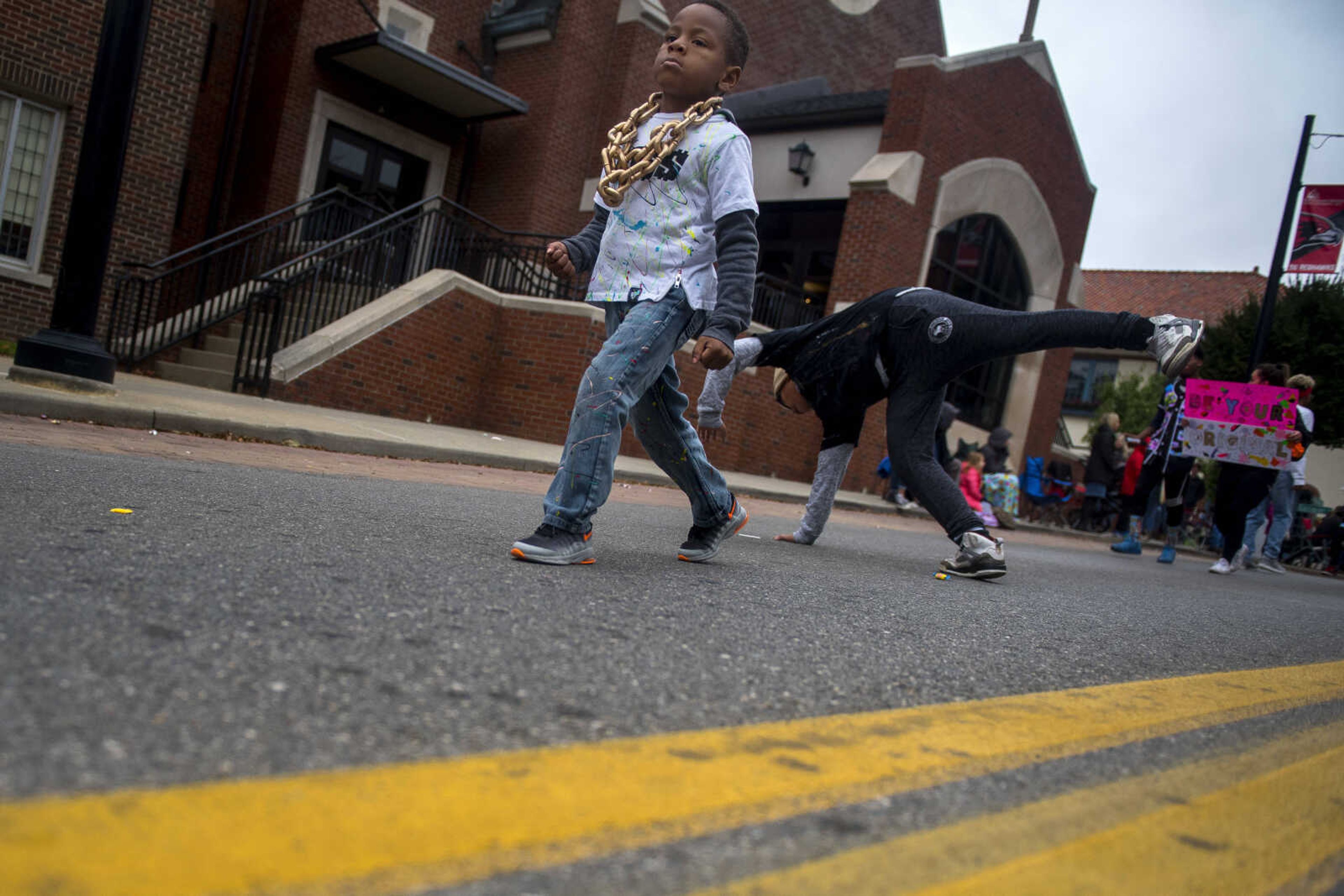 A young boy walks as his compatriot breakdances in the street during the Southeast Missouri State University homecoming parade Saturday, Oct. 13, 2018.