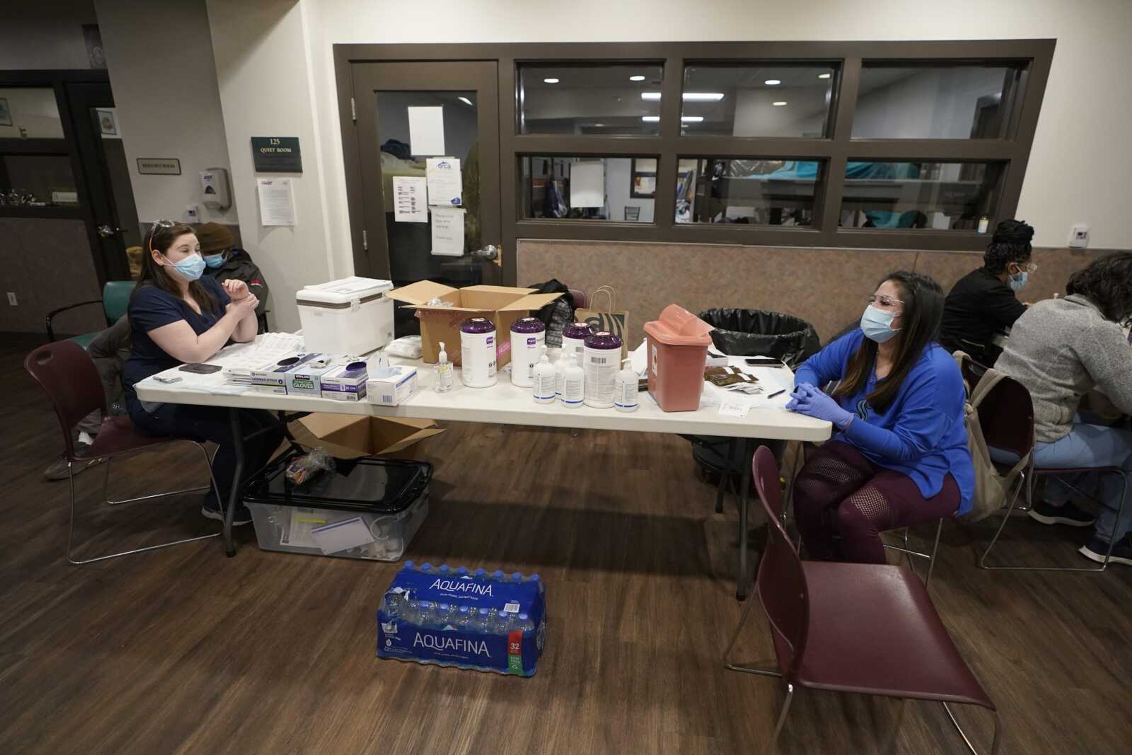 Aurora Artman, right, a medical assistant at Harborview Medical Center, talks with a colleague as they work Wednesday at a COVID-19 vaccination clinic set up at a YWCA shelter for women lacking housing in Seattle.