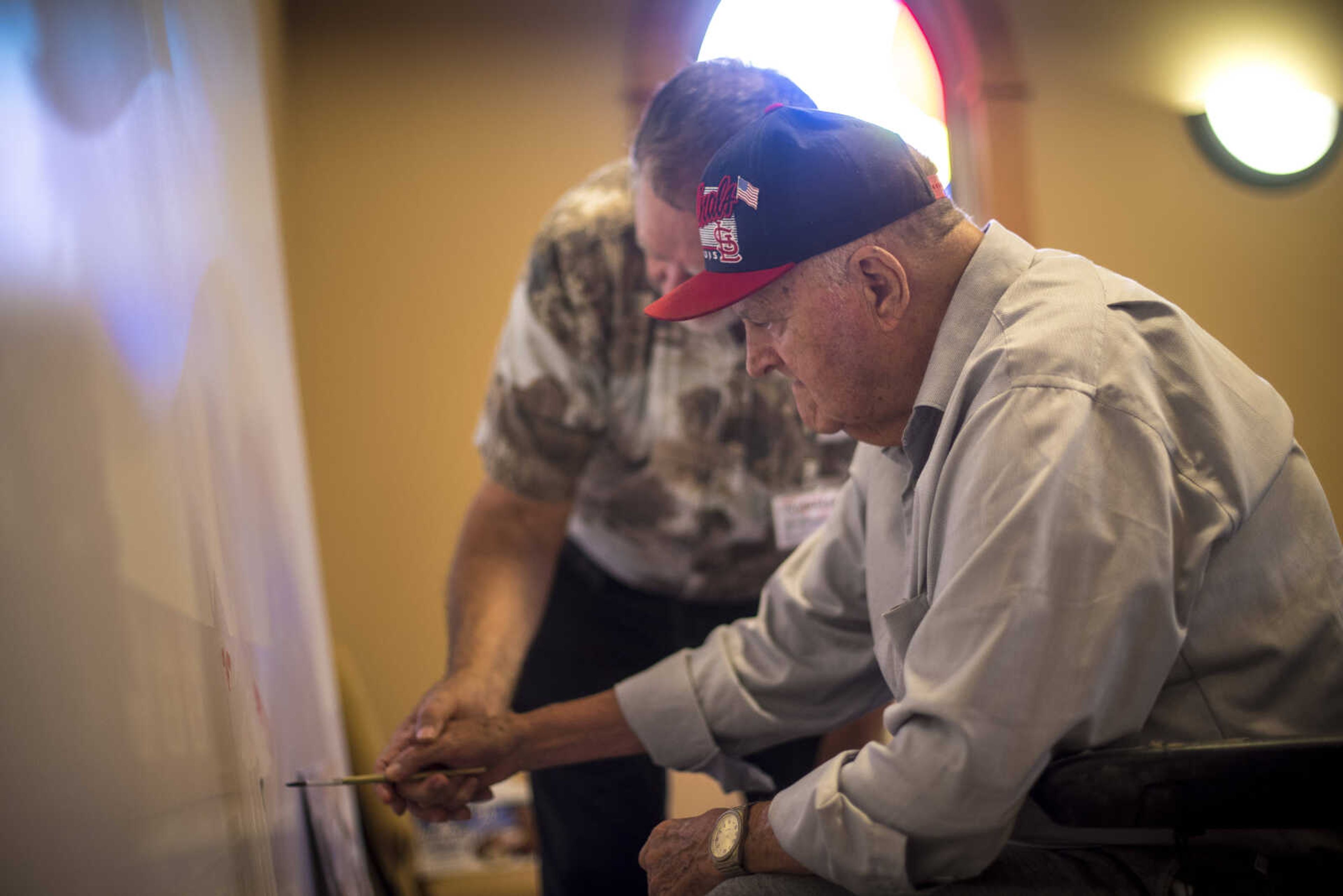 Gus Gockel paints a large canvas guided by Aaron Horrell for Paint-For-A-Cause where the residents of the Missouri Veterans Home will be given the opportunity to paint first on the big image Friday, July 28, 2017 in Cape Girardeau. Aaron Horrell will then take the painting to the SEMO District Fair where people can also help paint to raise money for the home.