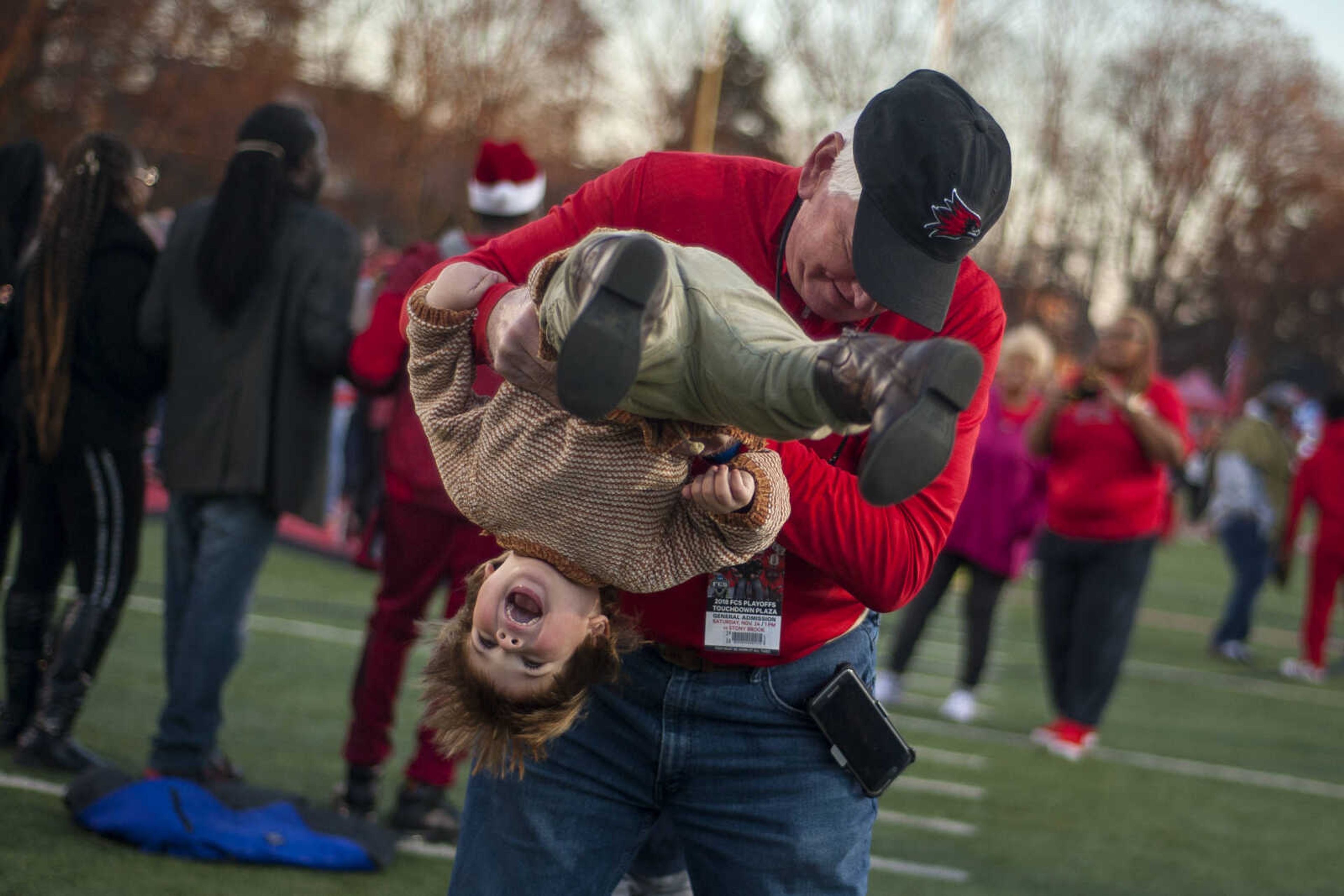 Dave Rigdon flips Fisher Ford, 2, on the field as fans celebrate the Redhawks' victory in their first-ever postseason game at Houck Stadium Saturday, Nov. 24, 2018.