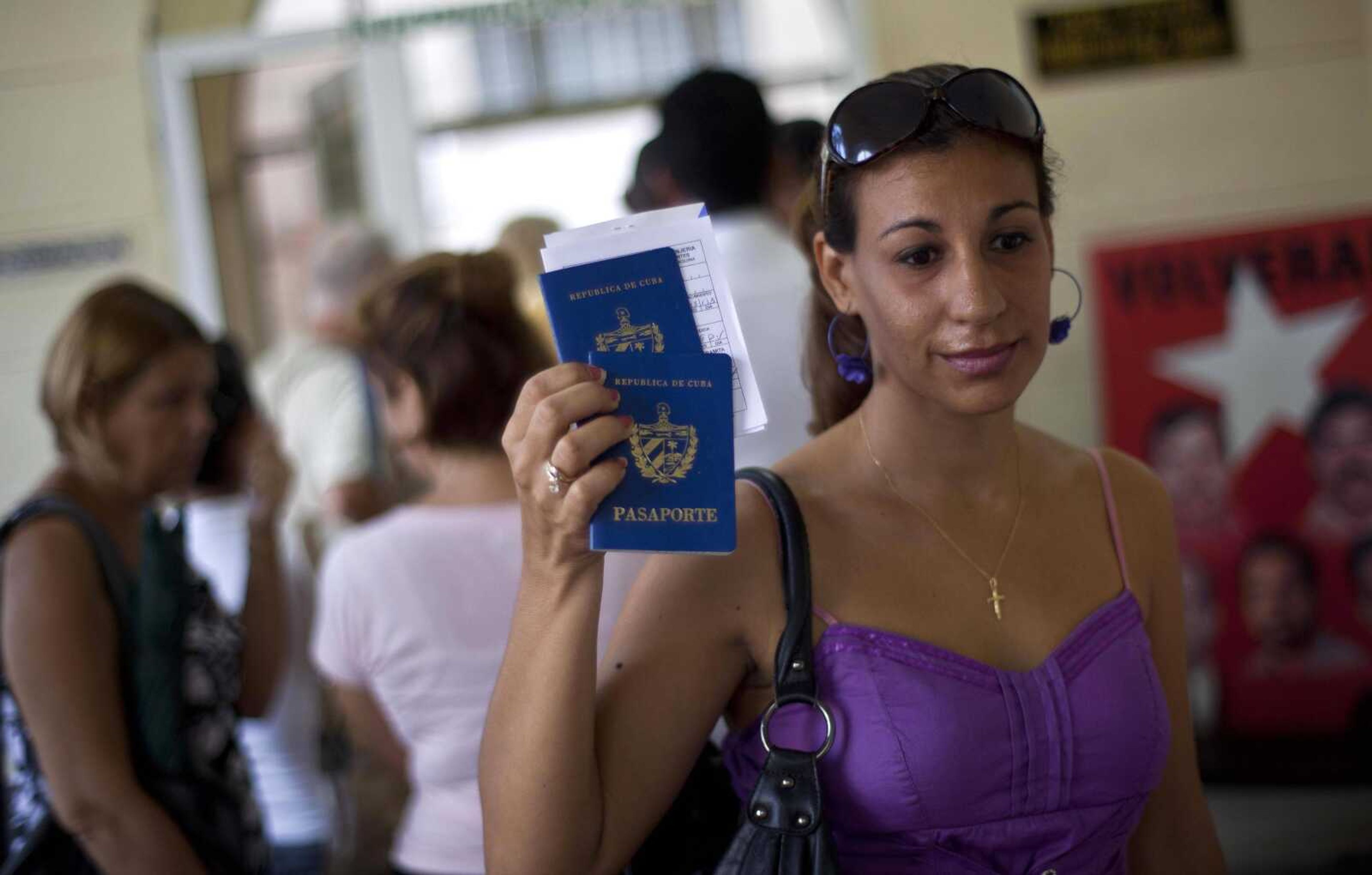 A woman shows her passport and that of her son to reporters Tuesday as she leaves an immigration office in Havana. The Cuban government announced Tuesday that it will no longer require islanders to apply for an exit visa, eliminating a much-loathed bureaucratic procedure that has been a major impediment for many seeking to travel overseas for more than a half-century. (Ramon Espinosa ~ Associated Press)