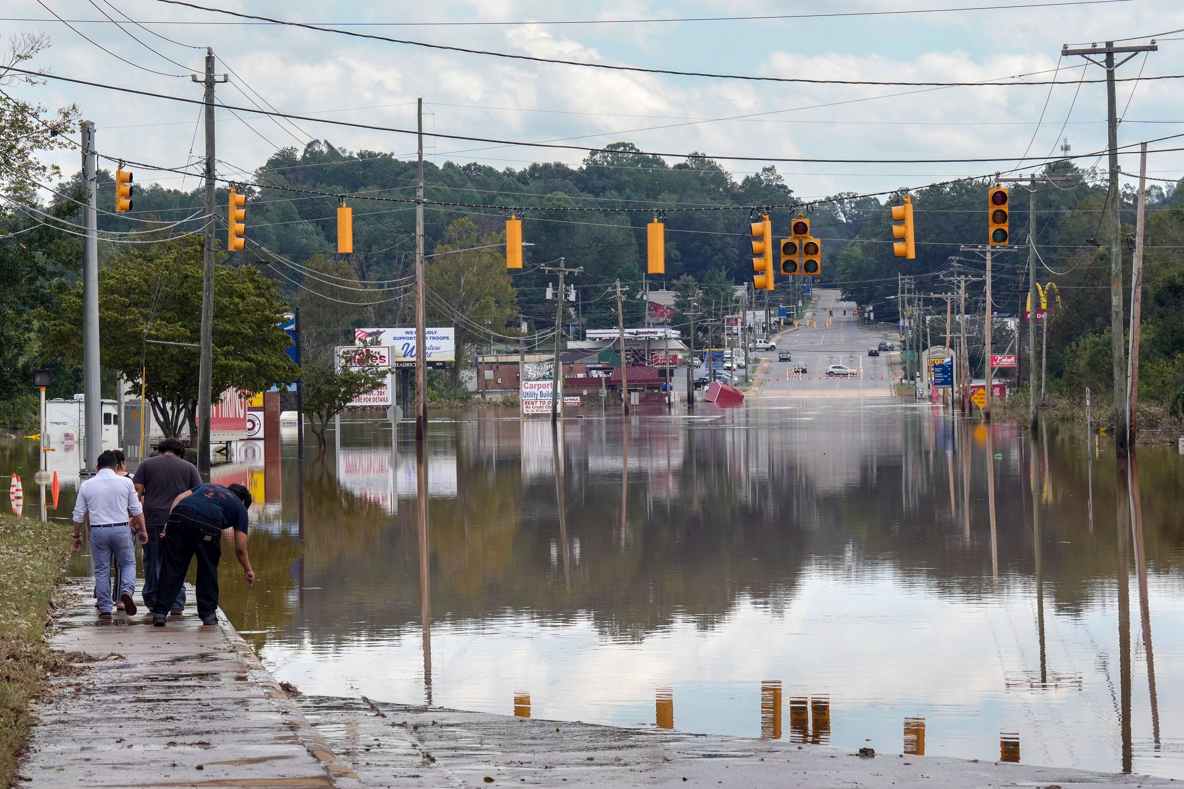 A passerby checks the water depth of a flooded road, Saturday, Sept. 28, 2024, in Morganton, N.C. Torrential rain from Hurricane Helene left many area streets flooded. In addition, traffic lights are inoperable due to no power, with downed power lines and trees. (AP Photo/Kathy Kmonicek)