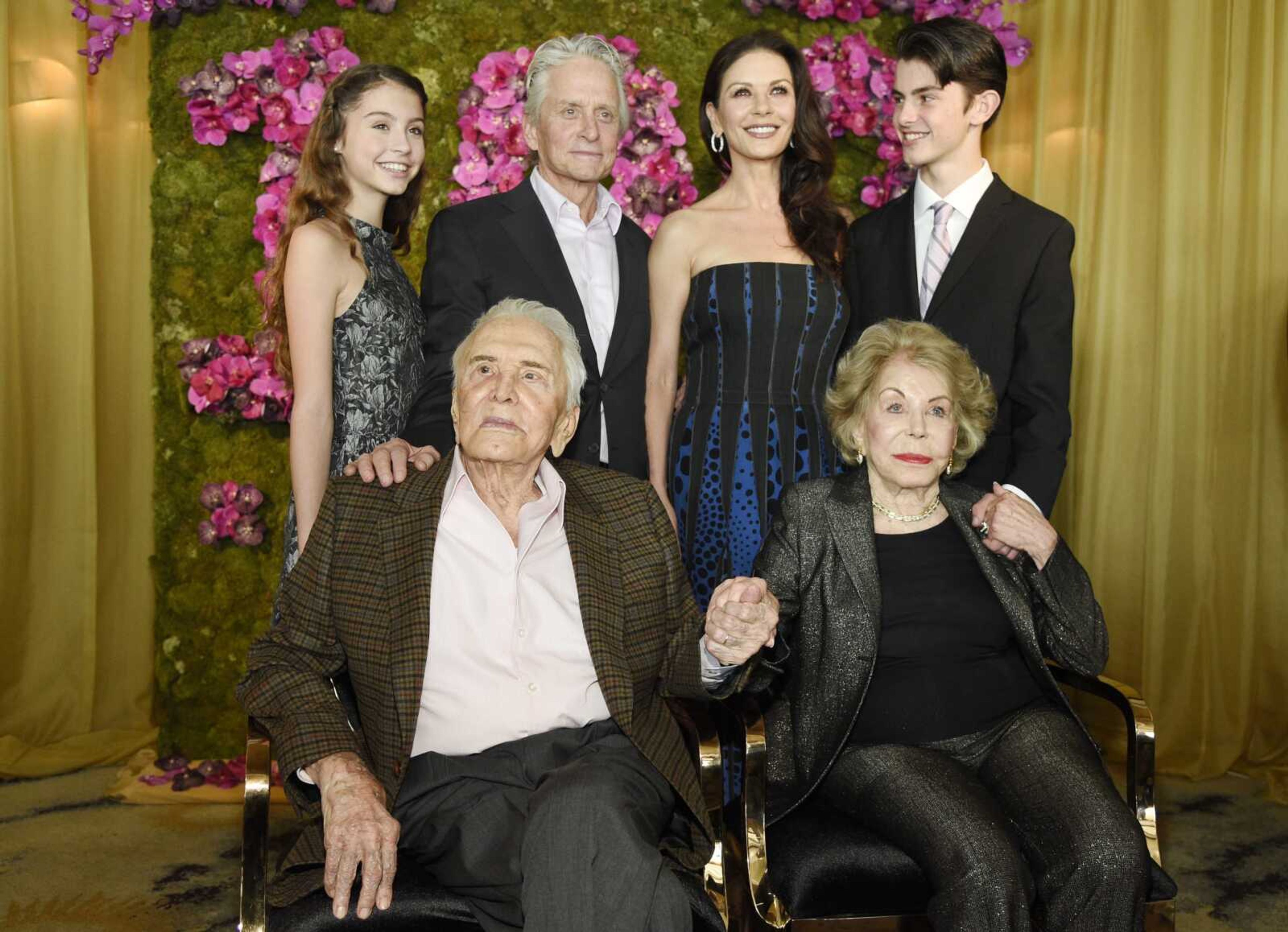 Actor Kirk Douglas, seated left, holds hands with his wife, Anne, seated right, as they pose with family members, their son Michael, standing second left, his wife, Catherine Zeta-Jones, standing second and their children, Carys, left, and son Dylan during Kirk's 100th birthday party in Beverly Hills, California. Kirk Douglas died Wednesday at age 103.