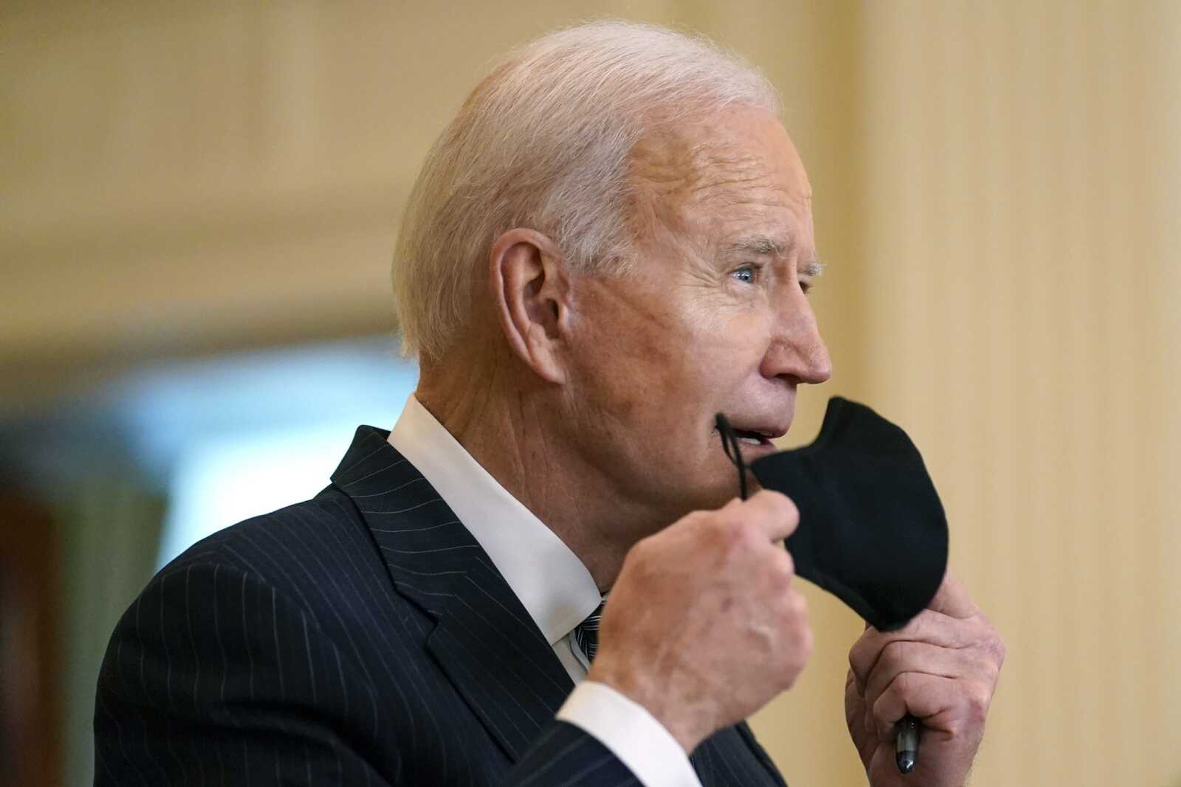 President Joe Biden removes his face mask as he arrives Thursday to speak about COVID-19 vaccinations in the East Room of the White House.