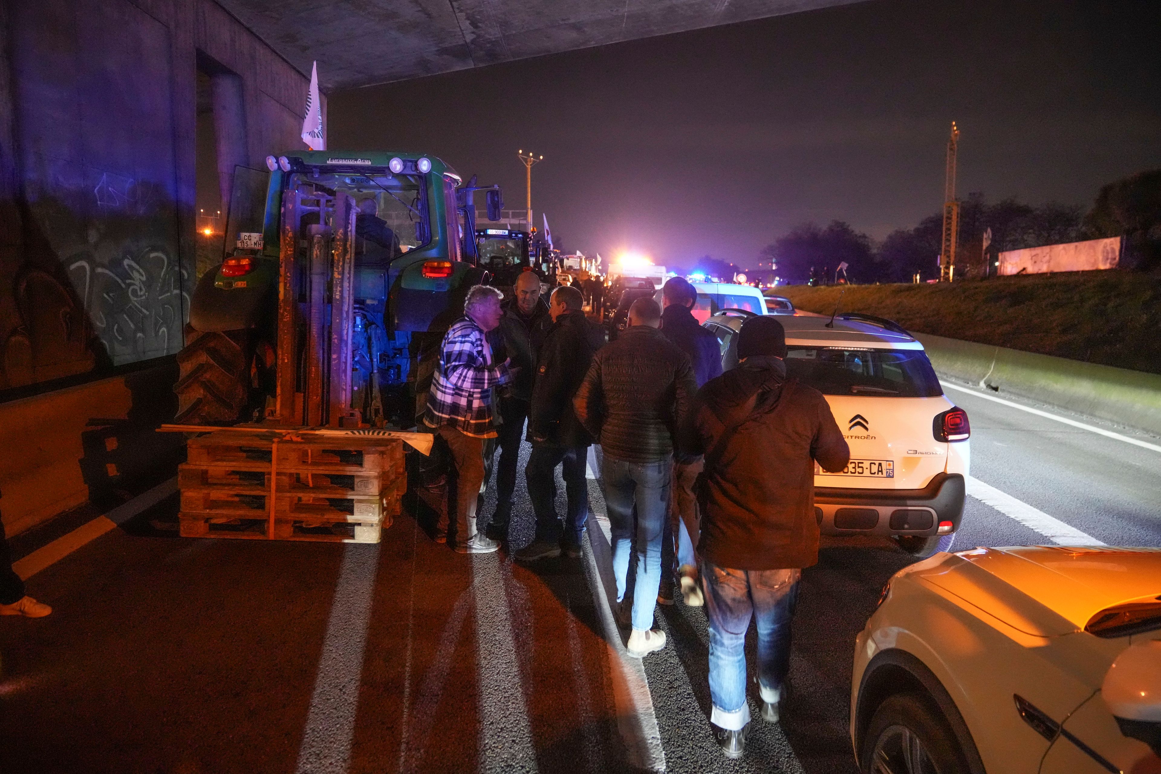 Farmers walk between tractors and cars on a blocked highway in Velizy-Villacoublay, outside Paris, Sunday, Nov. 17, 2024. (AP Photo/Michel Euler)