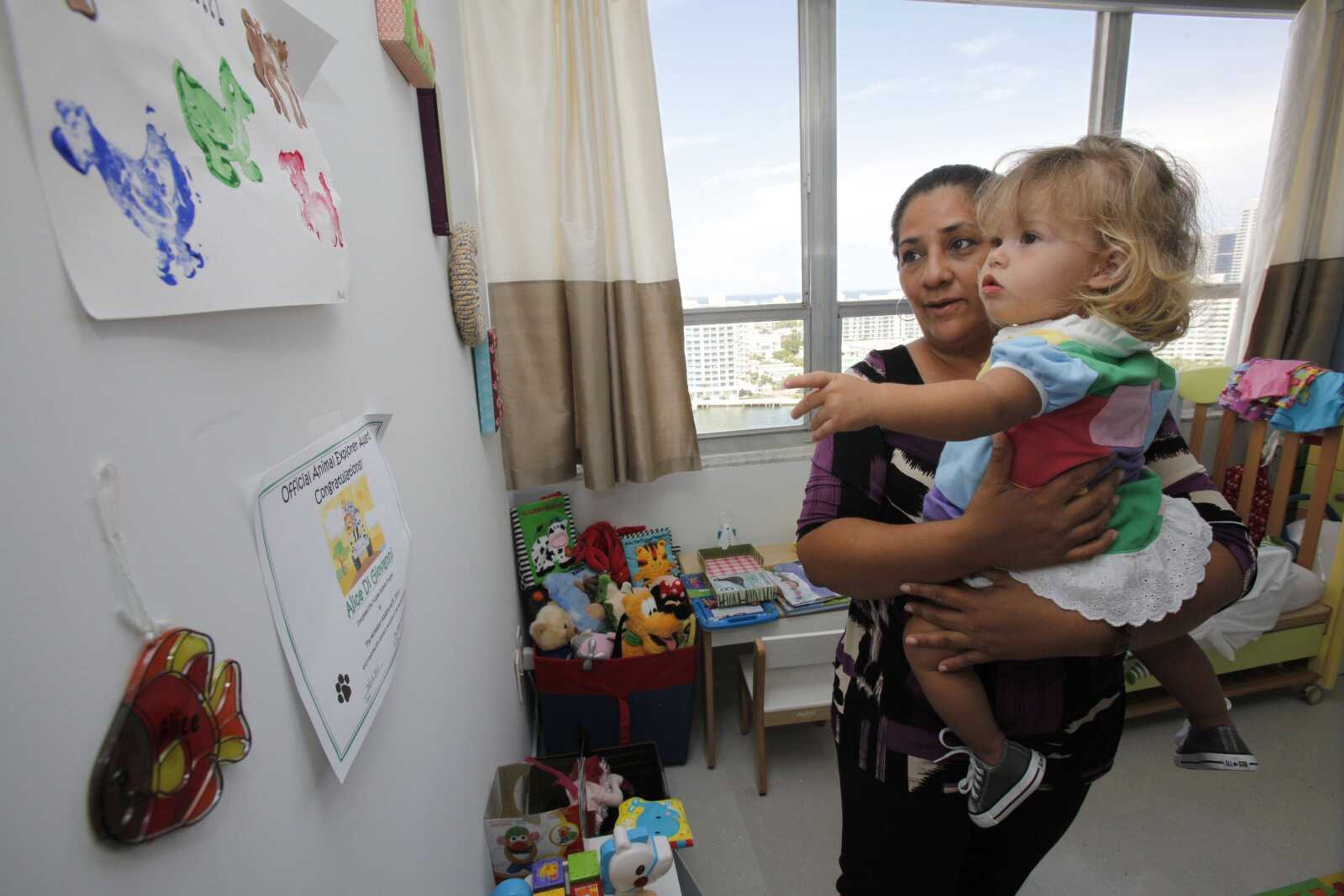 Alice Di Giovanni, 1, reaches for a drawing on a wall while she is held by her nanny Marisol Espinoza Lazo in Miami Beach, Fla. Alice is one of an increasing number of Americans living in homes where languages other than English are spoken. (Wilfredo Lee ~ Associated Press)