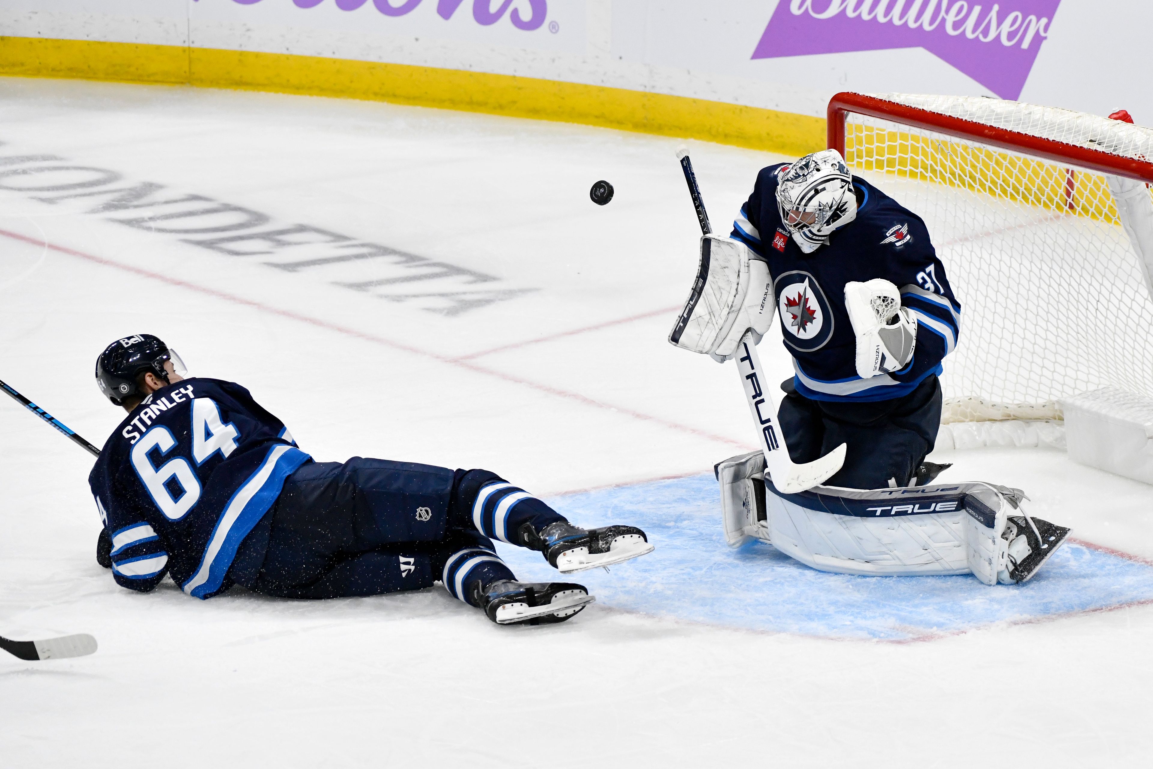 Winnipeg Jets goaltender Connor Hellebuyck (37) makes a save on a St. Louis Blues shot as Logan Stanley (64) slides in front of the net during the third period of their NHL hockey game in Winnipeg, Canada Tuesday, Dec. 3, 2024. (Fred Greenslade/The Canadian Press via AP)