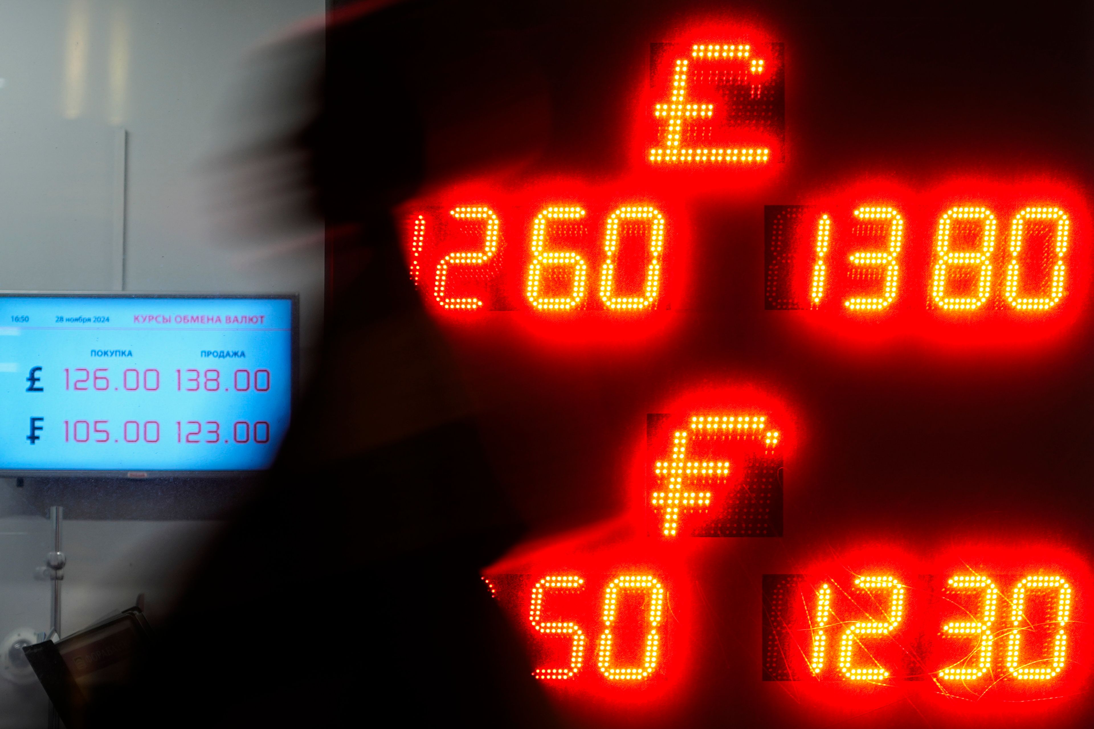 A pedestrian walks in a street near an exchange office sign showing the currency exchange rates of the Russian ruble, British pound sterling and Swiss franc in Moscow, Russia, Thursday, Nov. 28, 2024. (AP Photo/Pavel Bednyakov)