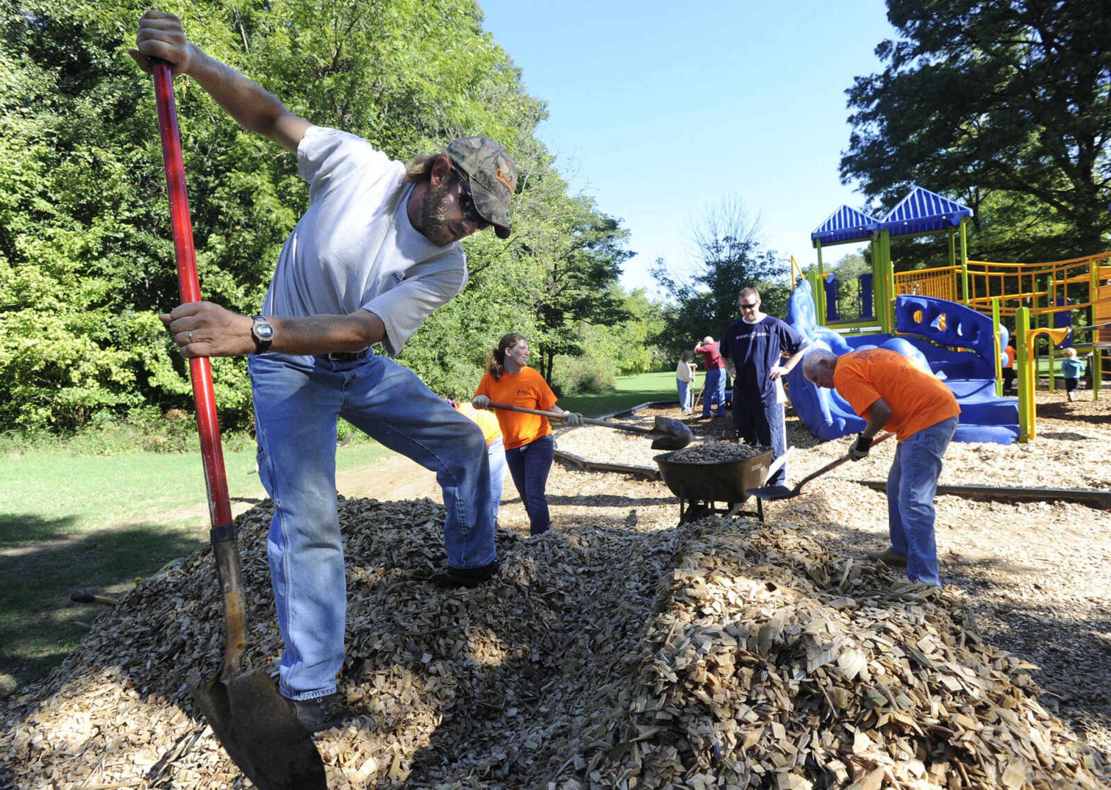 Matt Batchelor scoops wood chips with volunteers from Maple Avenue United Methodist Church for spreading at the new playground at Groves Park.