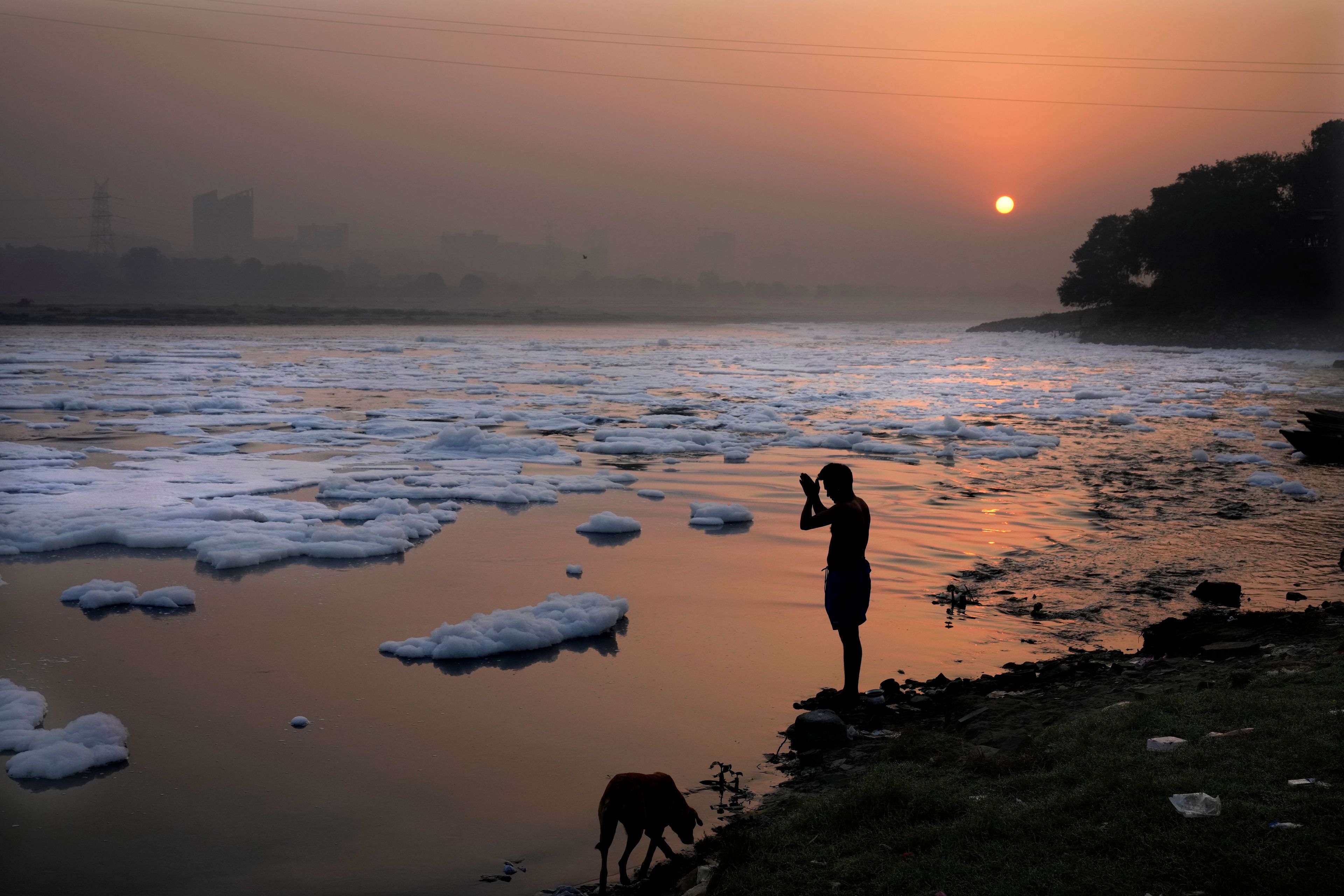 A person prays on the banks of the river Yamuna as toxic foams float in the river, in New Delhi, India, Tuesday, Oct. 29, 2024. (AP Photo/Manish Swarup)