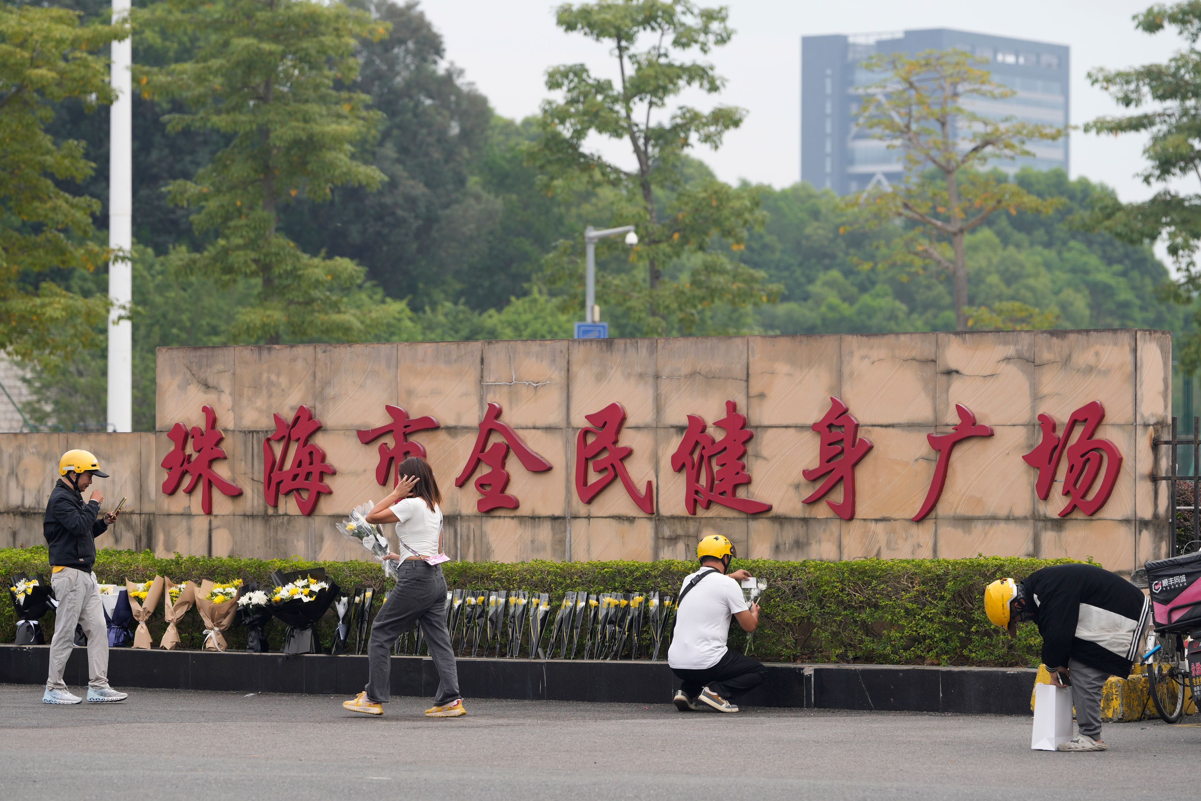 A woman walks past delivery men dropping off flowers outside the "Zhuhai People's Fitness Plaza" where a man rammed his car into people exercising at the sports center, in Zhuhai in southern China's Guangdong province on Wednesday, Nov. 13, 2024. (AP Photo/Ng Han Guan)