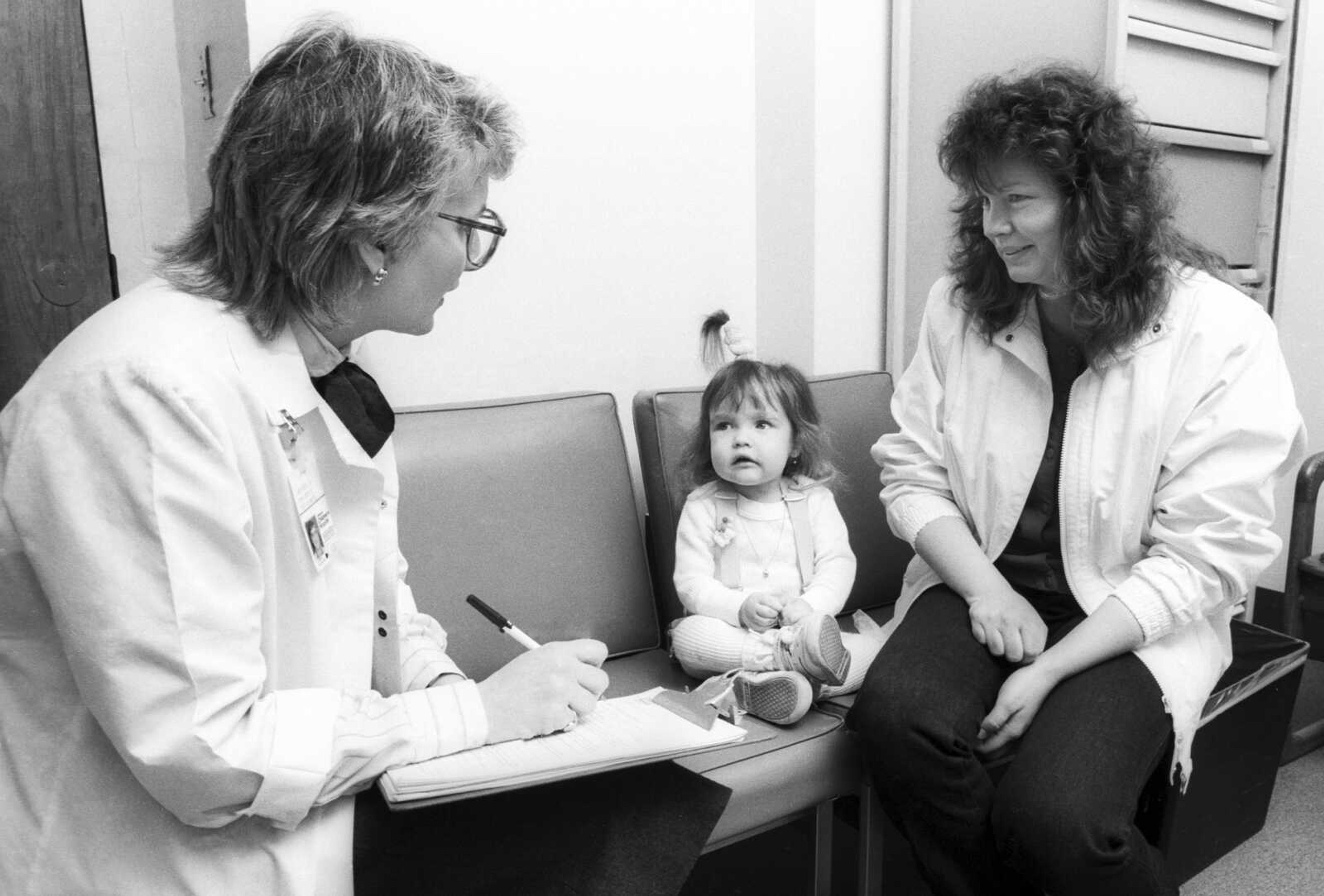 Nicole Frye, center, looks up at Lynn Bartos, pediatric nurse for Children's Hospital of Wisconsin Gastroenterology Clinic, left, at Children's Hospital of Wisconsin in Wauwatosa, Wisconsin. The nurse and family were featured on the cover of the hospital's nursing magazine in 1988 for a story about long term care. (Jeff Surges ~ Children's Hospital of Wisconsin via AP)