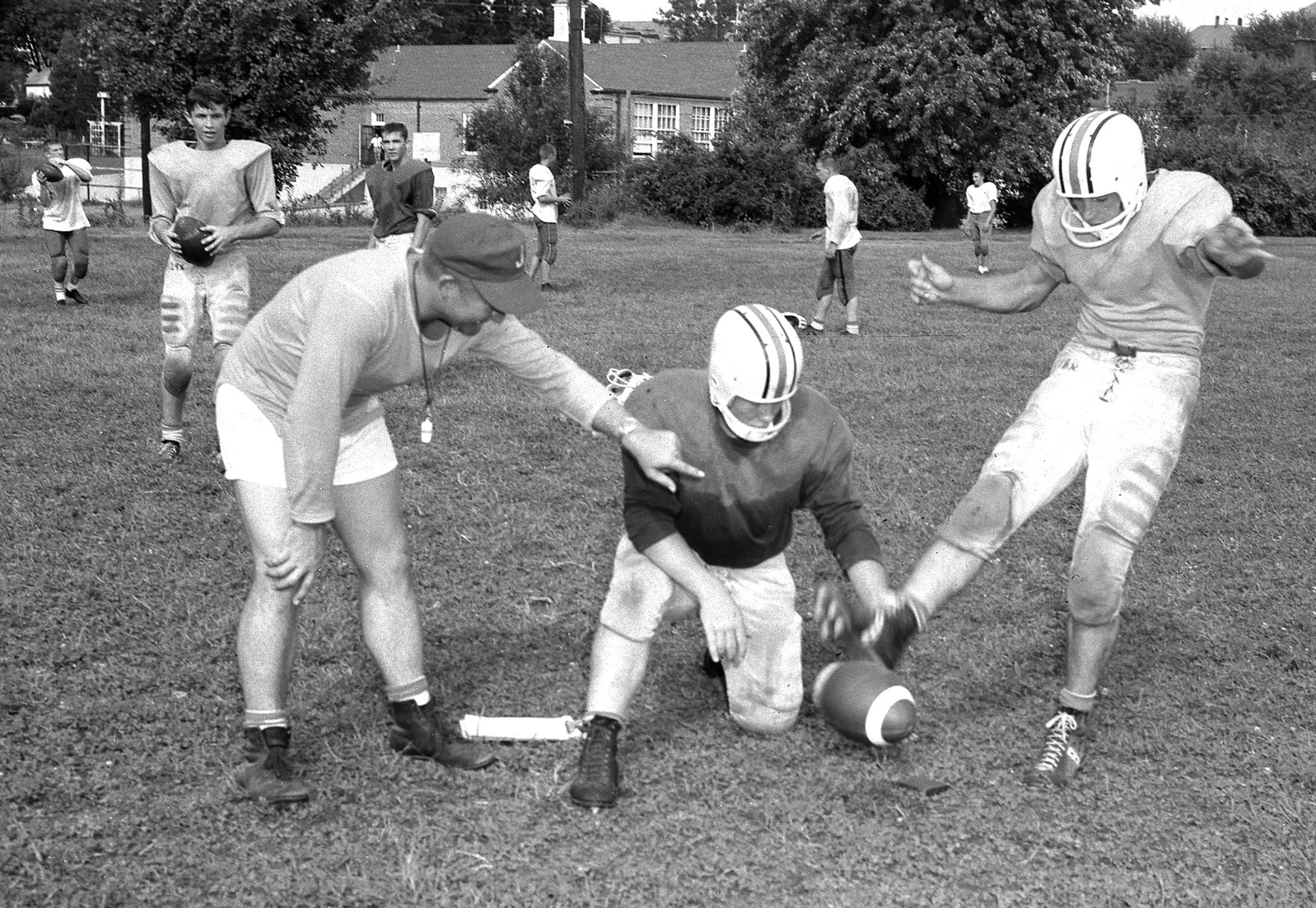 Jackson grid coach Mel Guemmer, left, gives pointer to Dennis Sievers, center, on holding a football for kicker Adolph Sokolowski on Sept. 13, 1961. 
