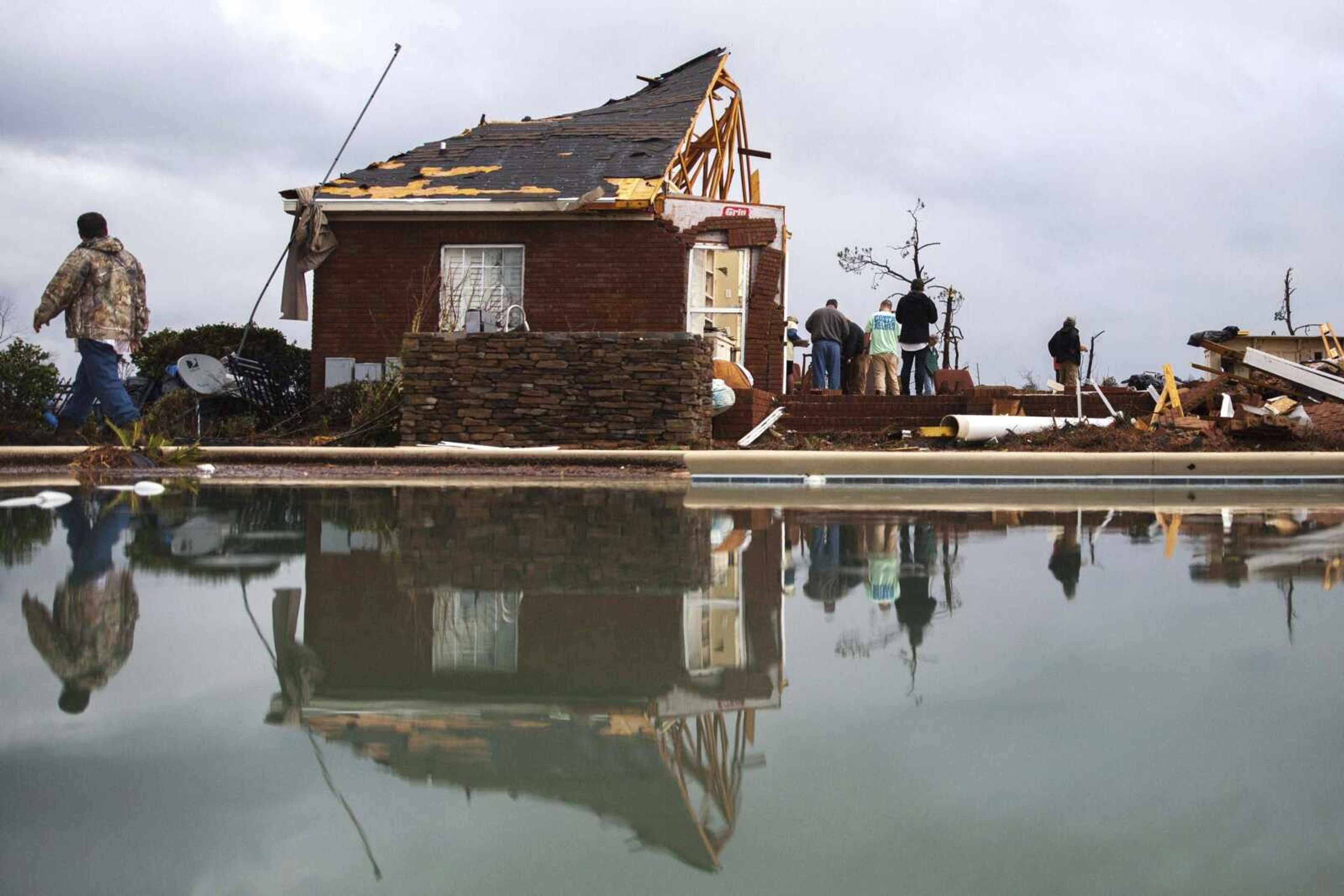 People are reflected in a swimming pool as they work to clean up at a home that was damaged by a tornado Sunday in Adel, Georgia.