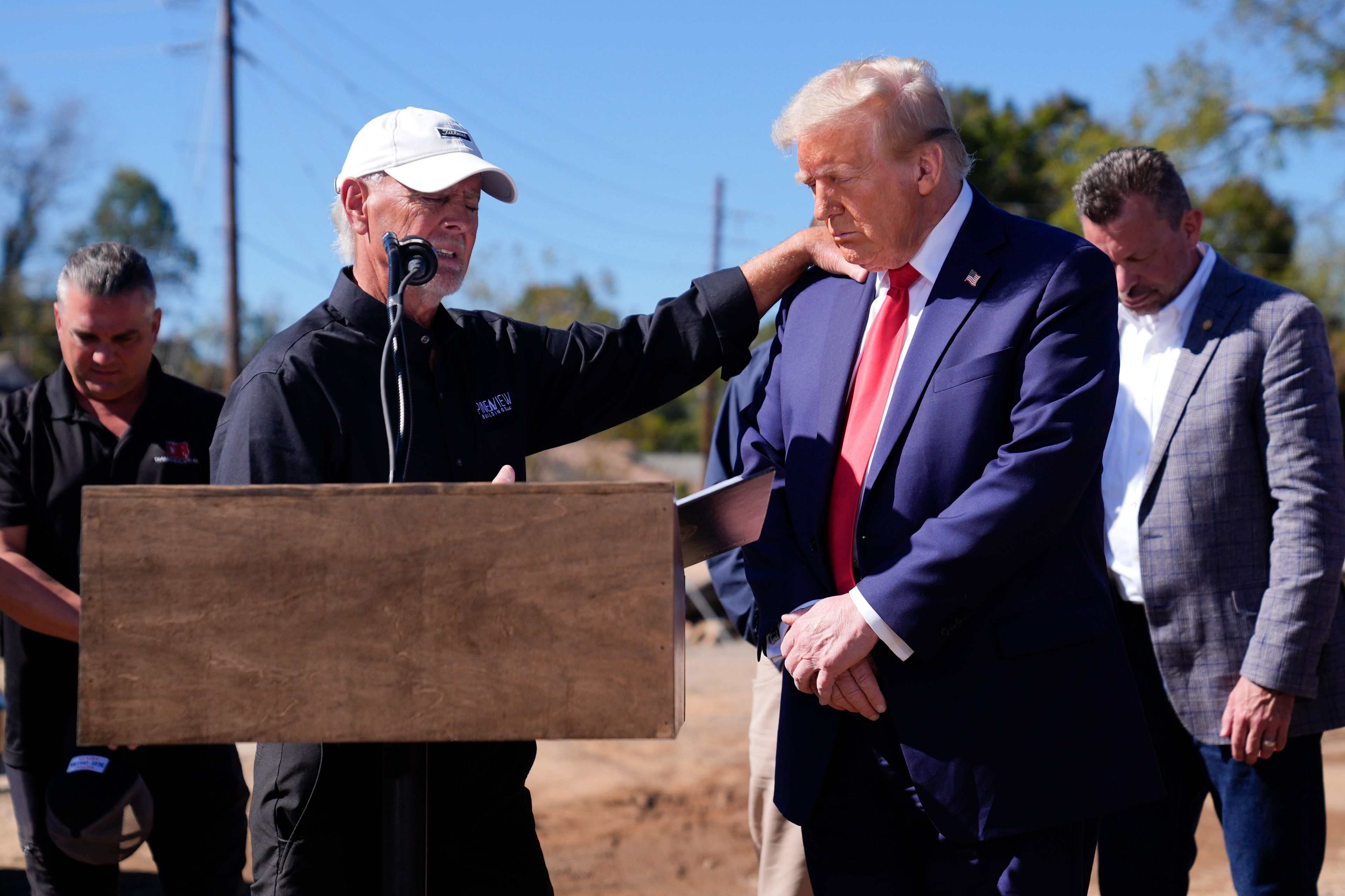 Republican presidential nominee former President Donald Trump prays with Mike Stewart, owner of Pine View Buildings, and others, after delivering remarks on the damage and federal response to Hurricane Helene, Monday, Oct. 21, 2024, in Swannanoa, N.C. (AP Photo/Evan Vucci)