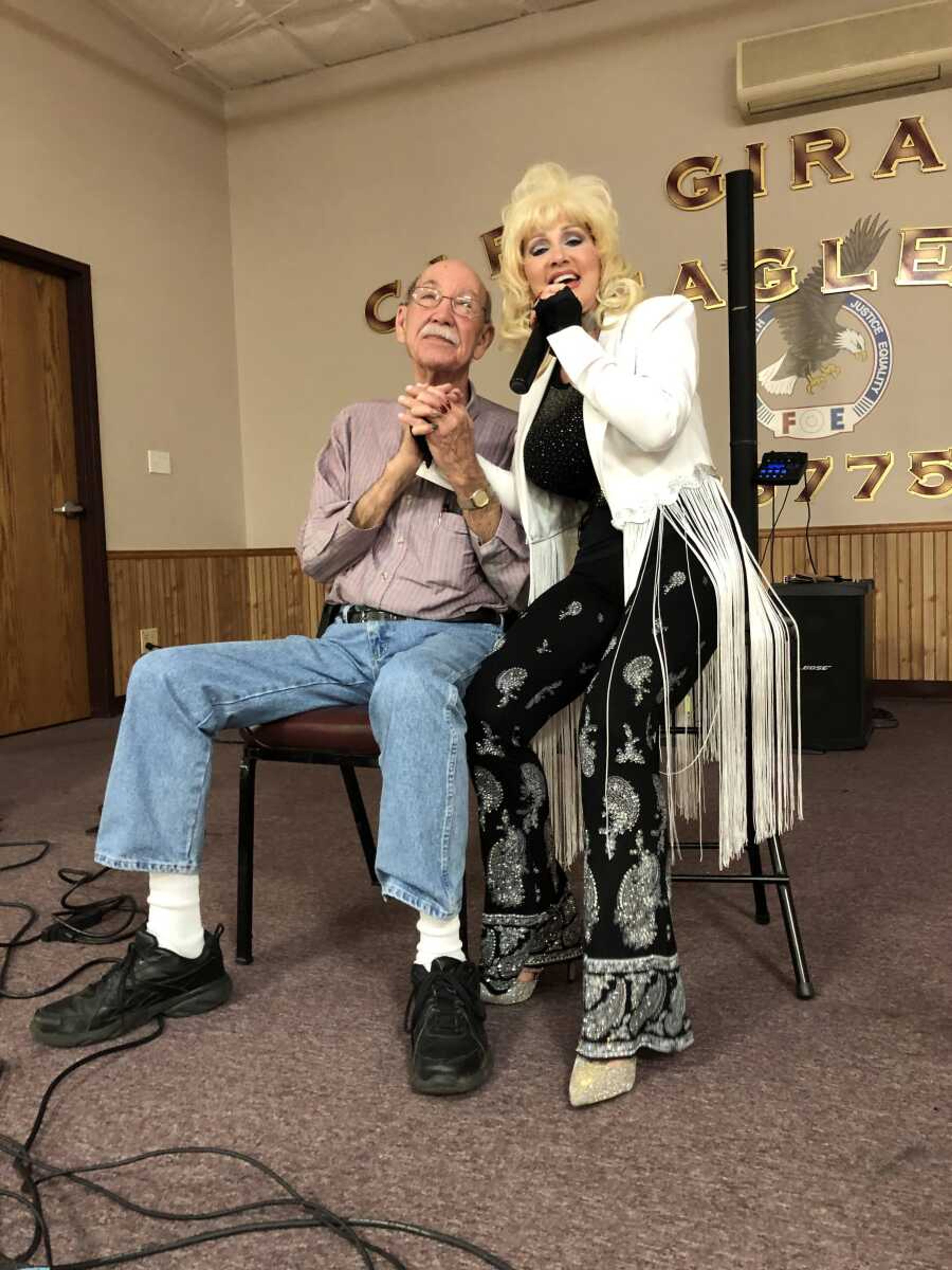 Therm Stull holds Dolly Parton Impersonator hand 
while she sings to him. 