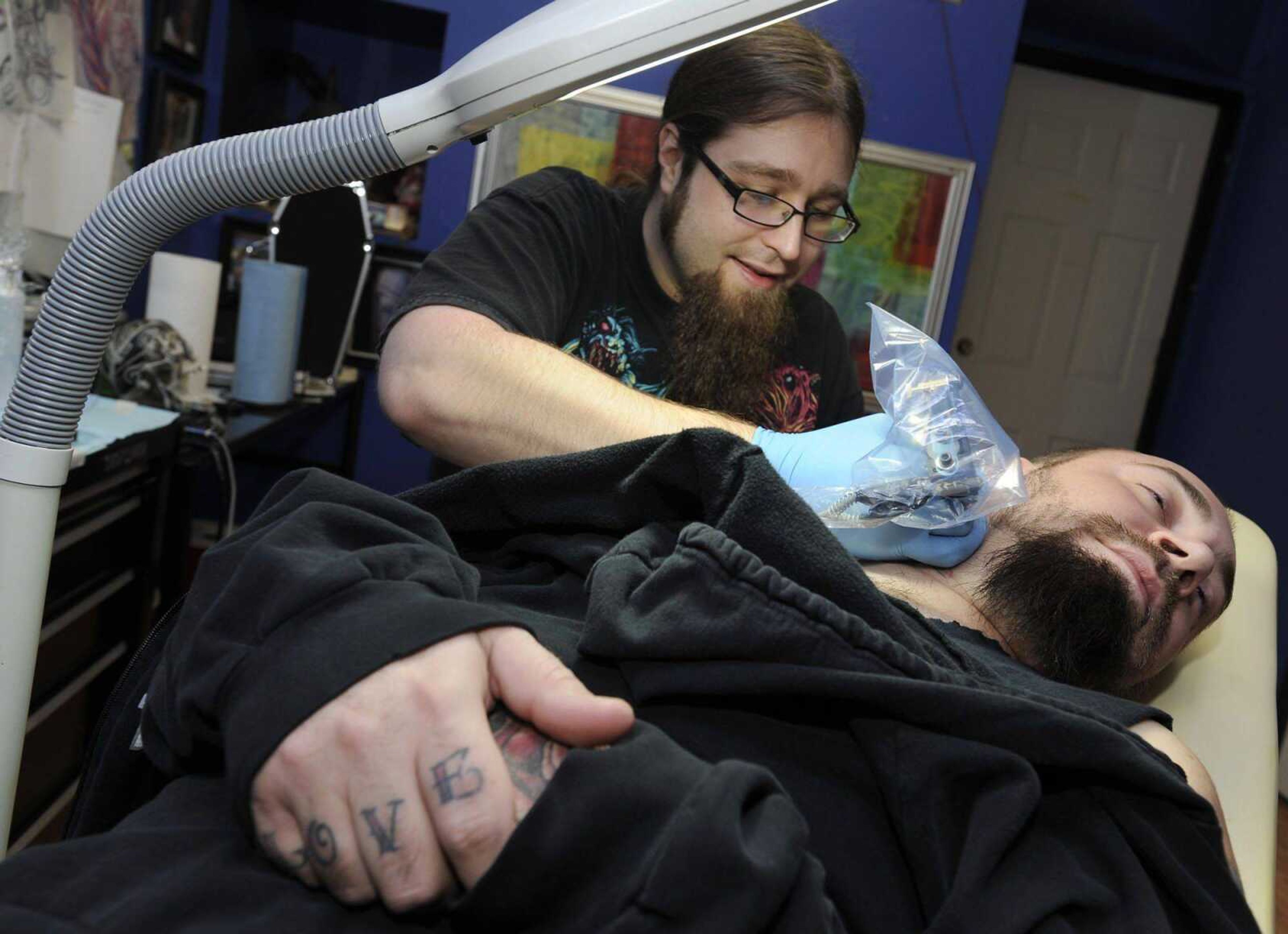 Andy Estes applies a tattoo on Chris Hester's neck Thursday at Flesh Hound in Cape Girardeau. Hester has been getting tattoos for 13 years. "Eventually he'll probably end up with a body suit," Estes said. (Fred Lynch)