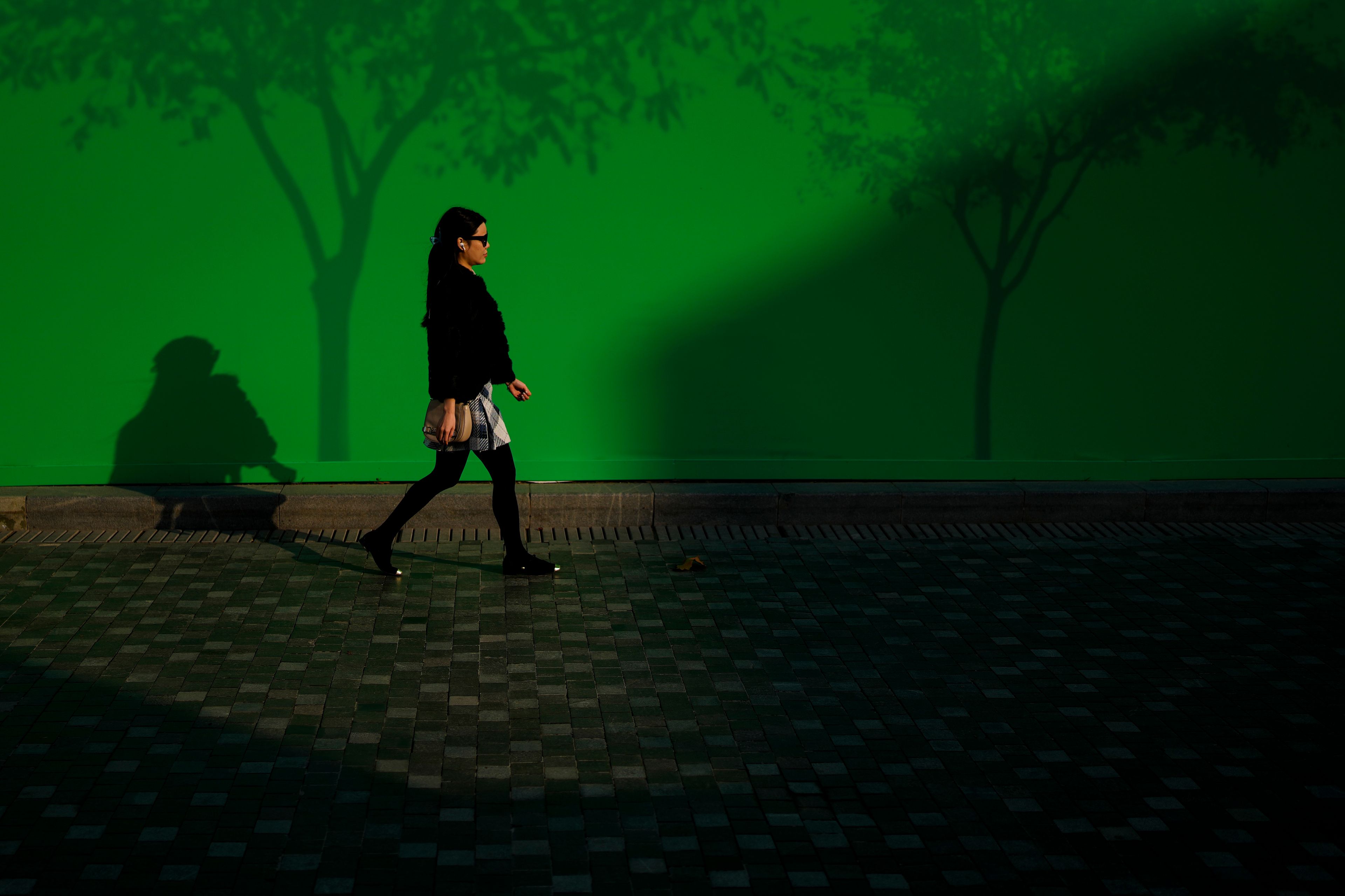 A woman walks by a board depicting trees outside a construction site at a popular outdoor shopping mall in Beijing, Thursday, Nov. 14, 2024. (AP Photo/Andy Wong)