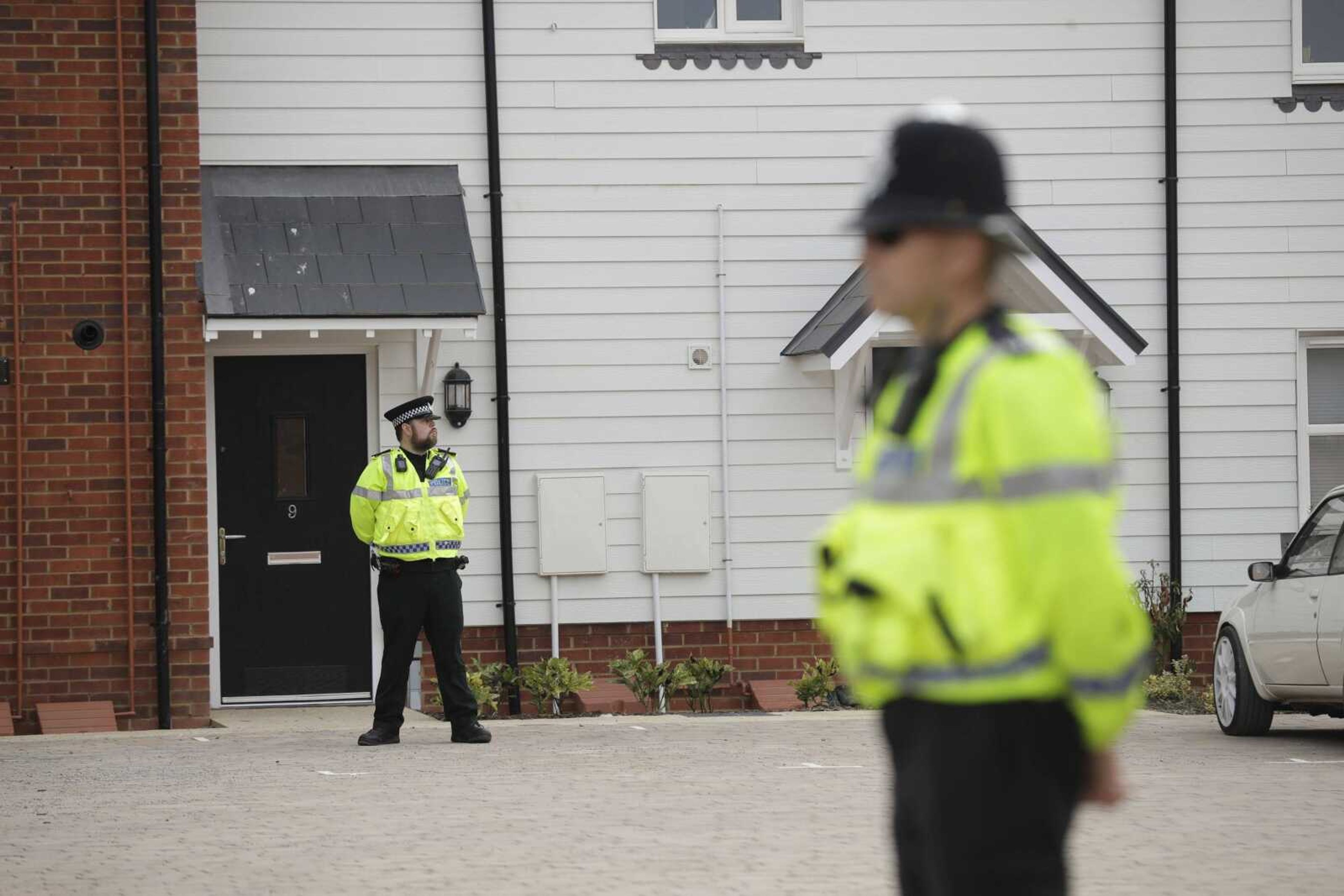 British police officers stand Wednesday outside the front door of a residential property in Amesbury, England. British police declared a "major incident" after two people were exposed to an unknown substance in the town and cordoned off places the people are known to have visited before falling ill.