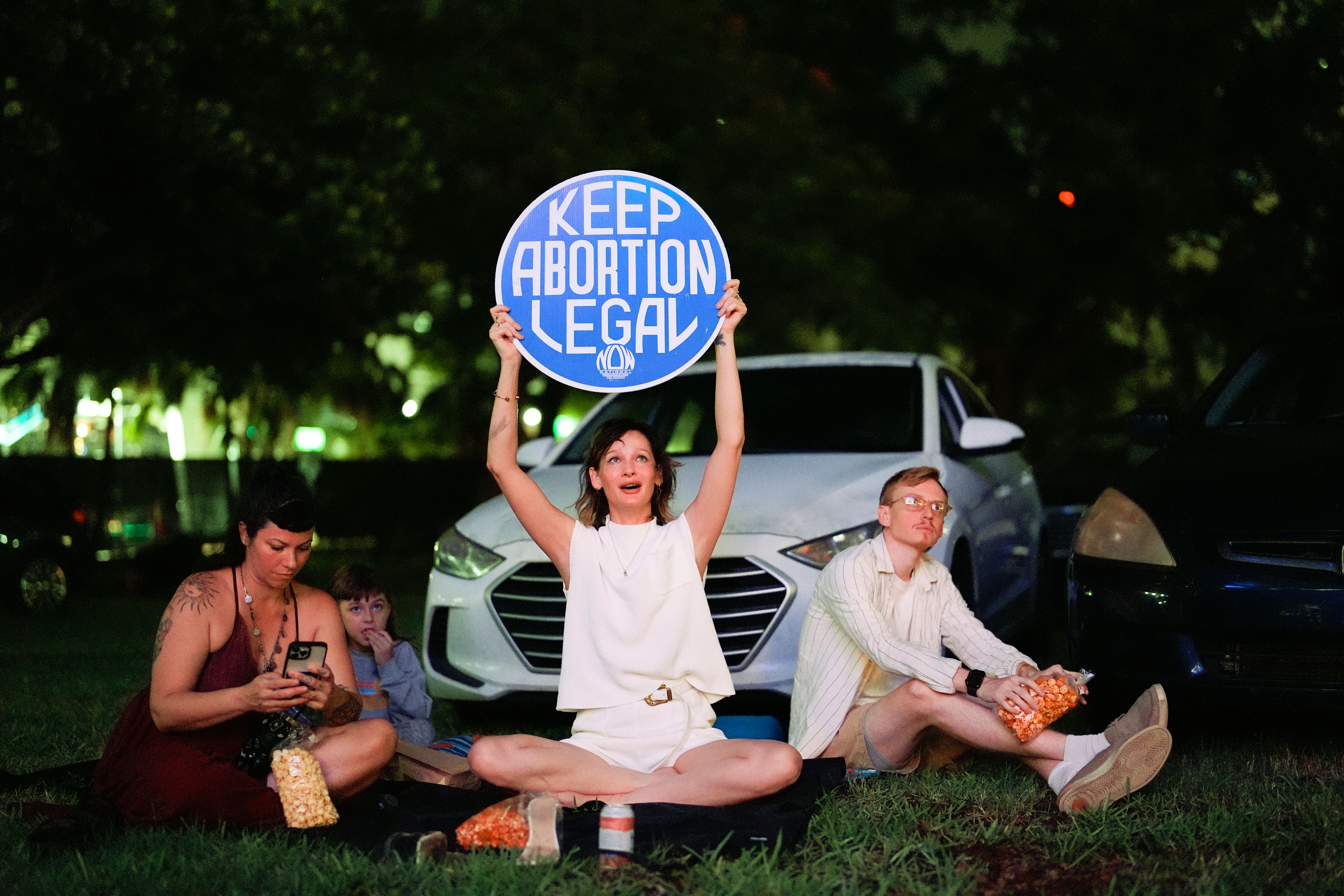 FILE - Reproductive rights advocate Kat Duesterhaus holds up a sign as U.S. President Joe Biden and his Republican rival, former President Donald Trump speak about abortion access, as the the first general election debate of the 2024 season is projected on a outdoor screen at the Nite Owl drive-in theater, Thursday, June 27, 2024, in Miami. (AP Photo/Rebecca Blackwell, File)