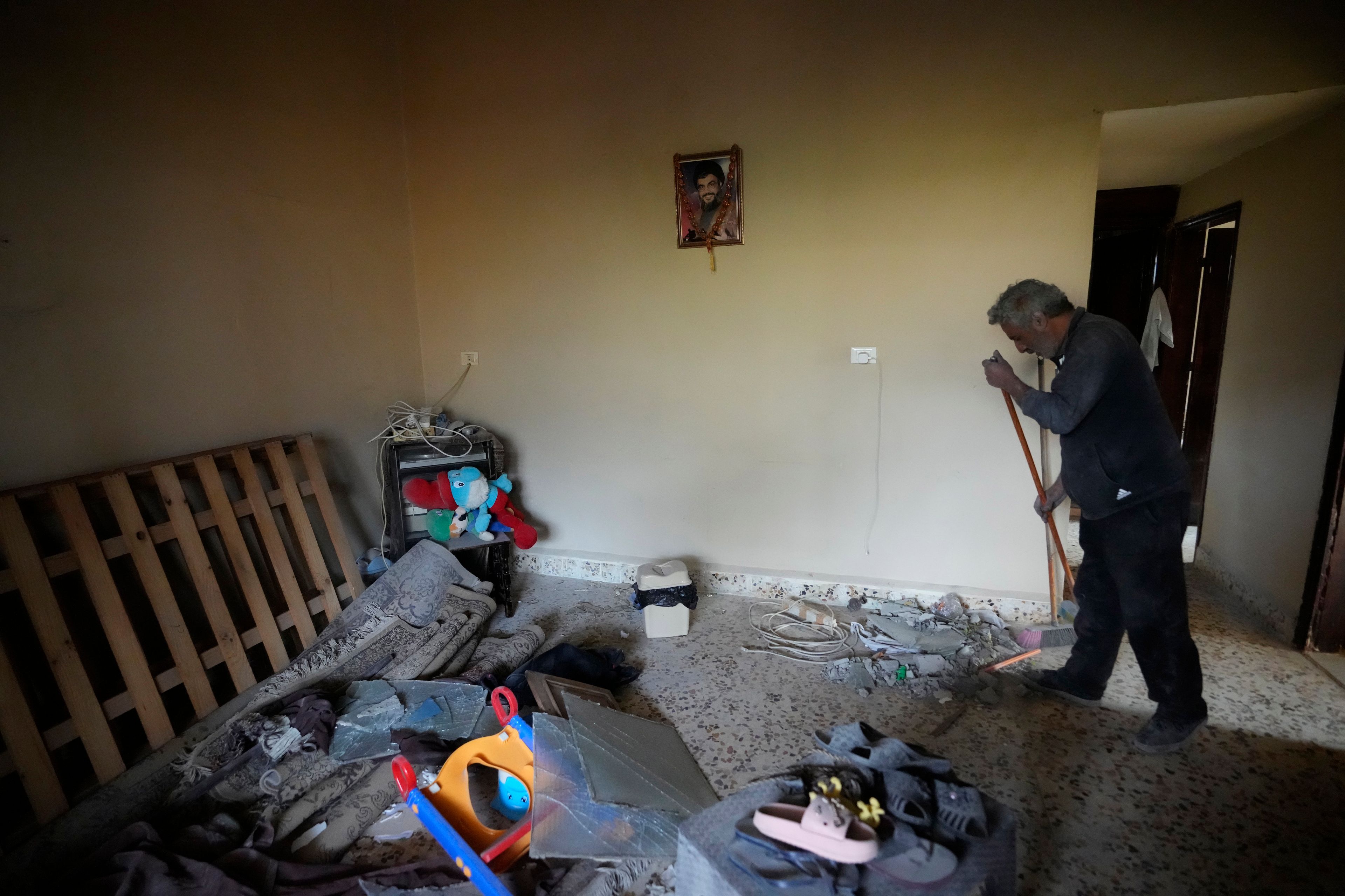 A man cleans a house, as a portrait hanging on the wall shows the late Hezbollah leader Sayyed Hassan Nasrallah, at the site where an Israeli airstrike hit a house in Aalmat village, northern Lebanon, Sunday, Nov. 10, 2024. (AP Photo/Hassan Ammar)