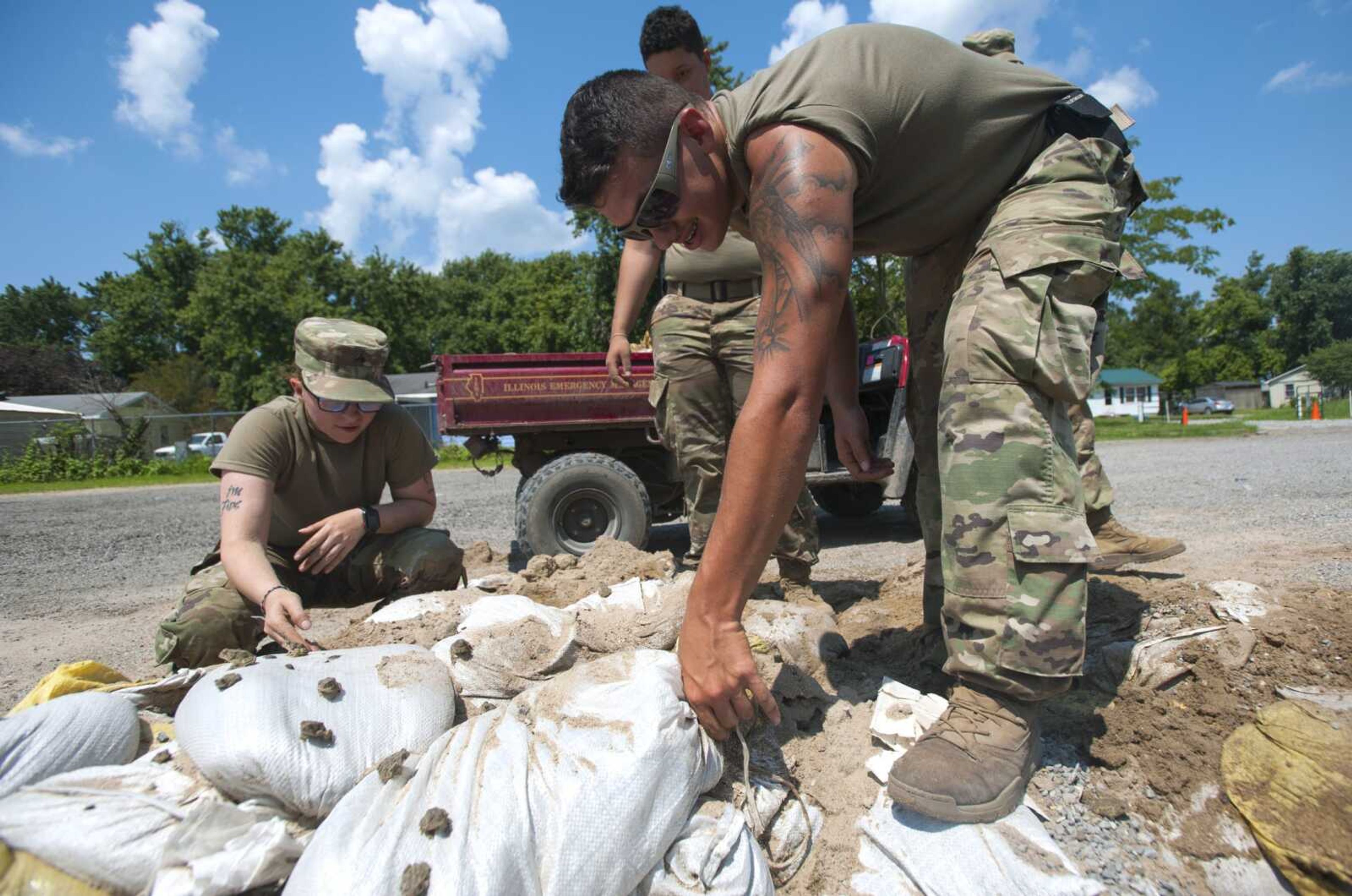 Illinois National Guard Cpl. Alyssa Artola, far left, crouches to inspect a group of frogs gathered atop a pile of sandbags as Illinois National Guard Spc. Albert Cook, front right, attempts to remove a bag from the pile Sunday in East Cape Girardeau, Illinois.