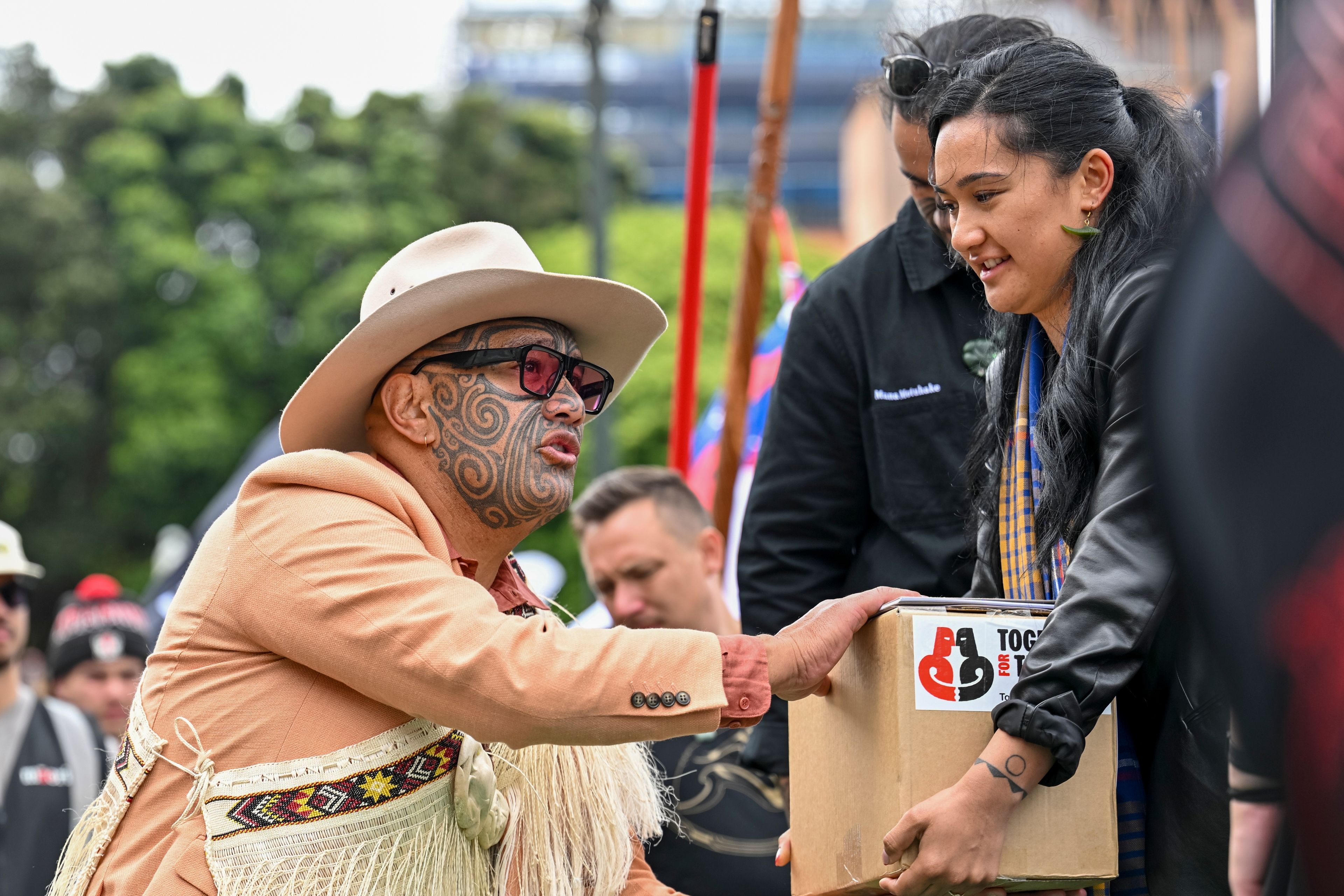 A petition is delivered to Member of Parliament Rawiri Waititi, left, outside New Zealand's parliament during a protest against a proposed law that would redefine the country's founding agreement between Indigenous Māori and the British Crown, in Wellington Tuesday, Nov. 19, 2024. (AP Photo/Mark Tantrum)