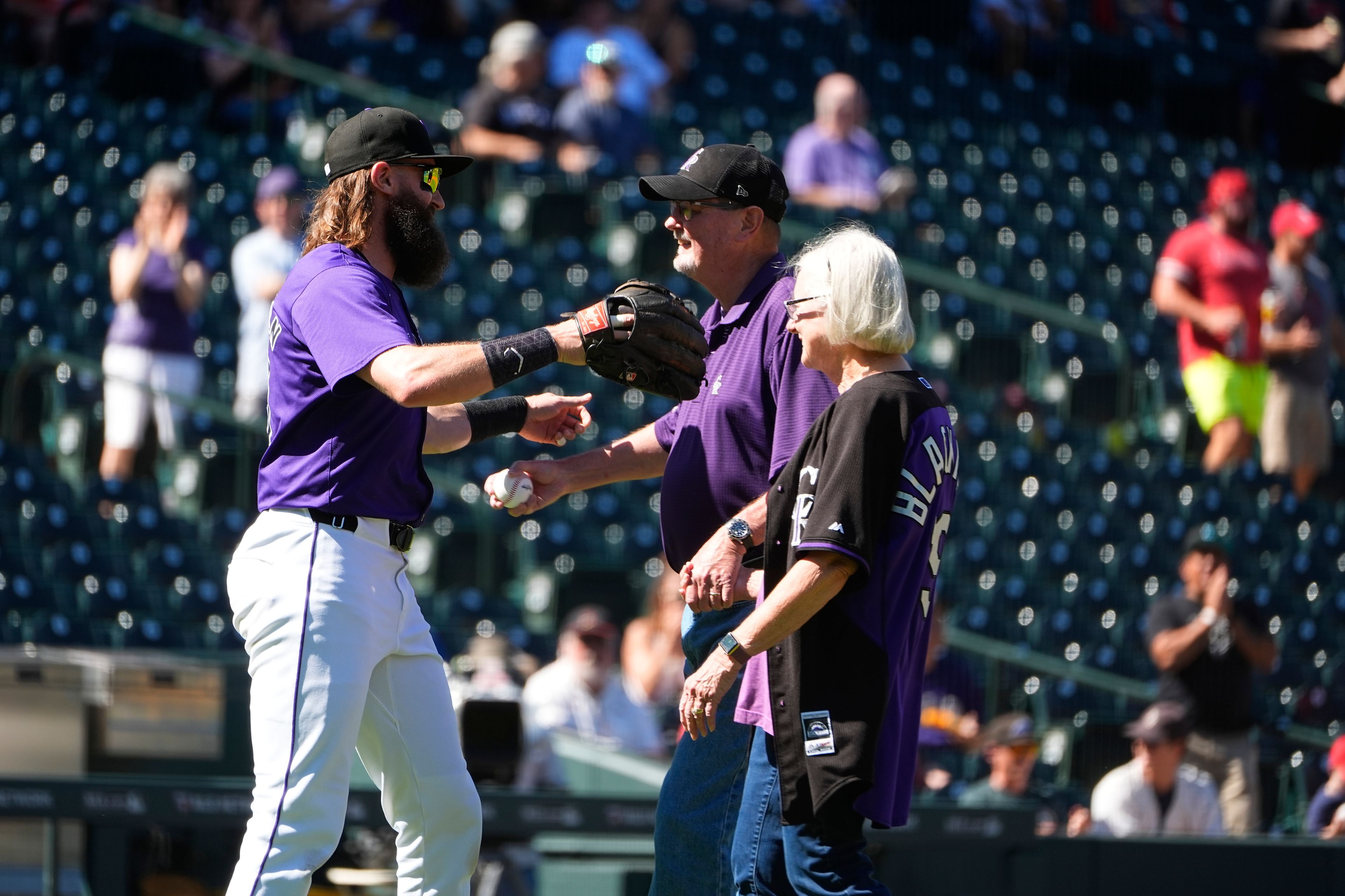 Colorado Rockies' Charlie Blackmon, left, who is retiring at season's end, hugs his father, Myron, back right, while his mother, Ellen, looks on after fielding a ceremonial first pitch from his parents before a baseball game against the St. Louis Cardinals Thursday, Sept. 26, 2024, in Denver. (AP Photo/David Zalubowski)