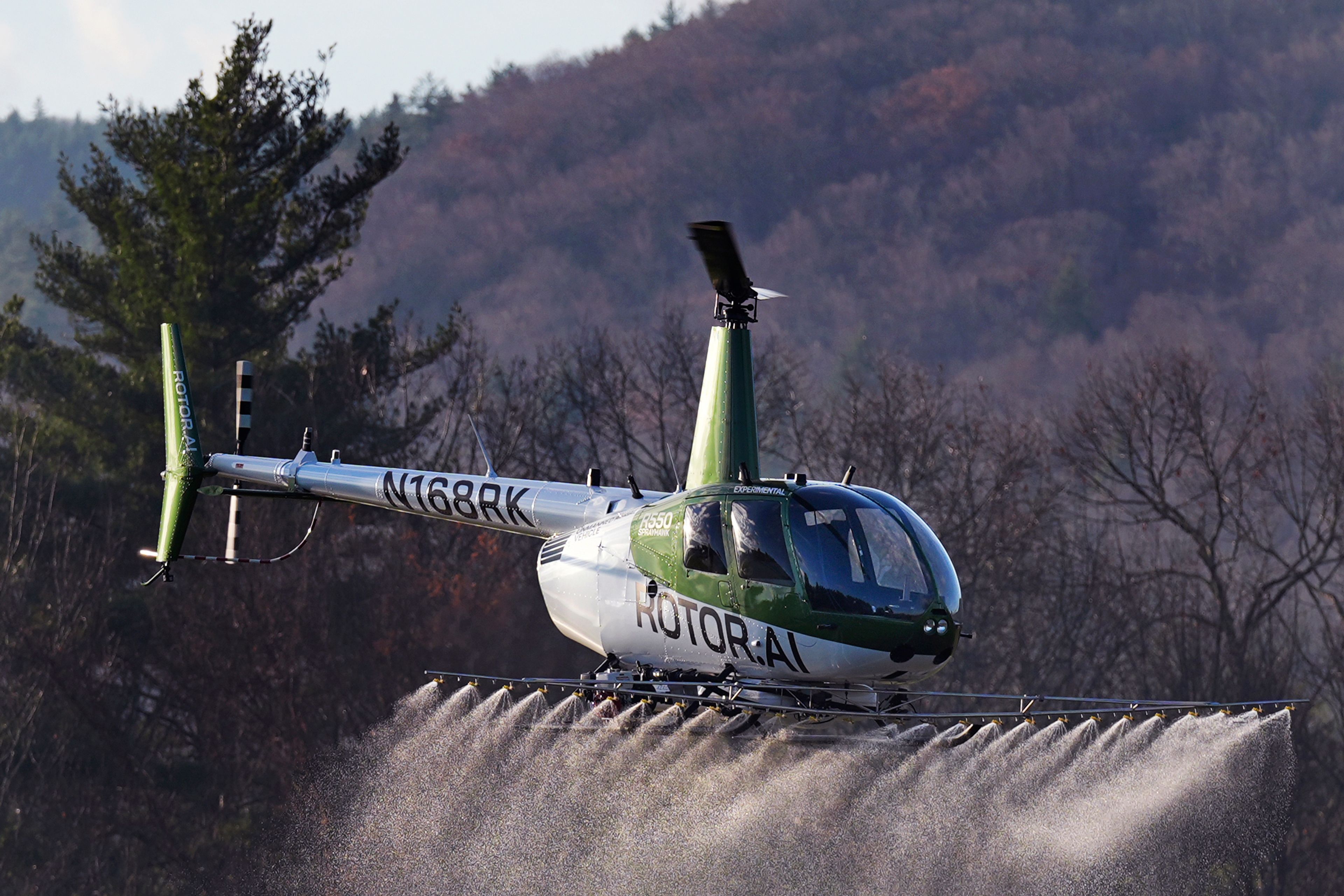 A Rotor Technologies unmanned semi-autonomous helicopter sprays a payload of water during a test flight over Intervale Airport, Monday, Nov. 11, 2024, in Henniker, N.H. (AP Photo/Charles Krupa)