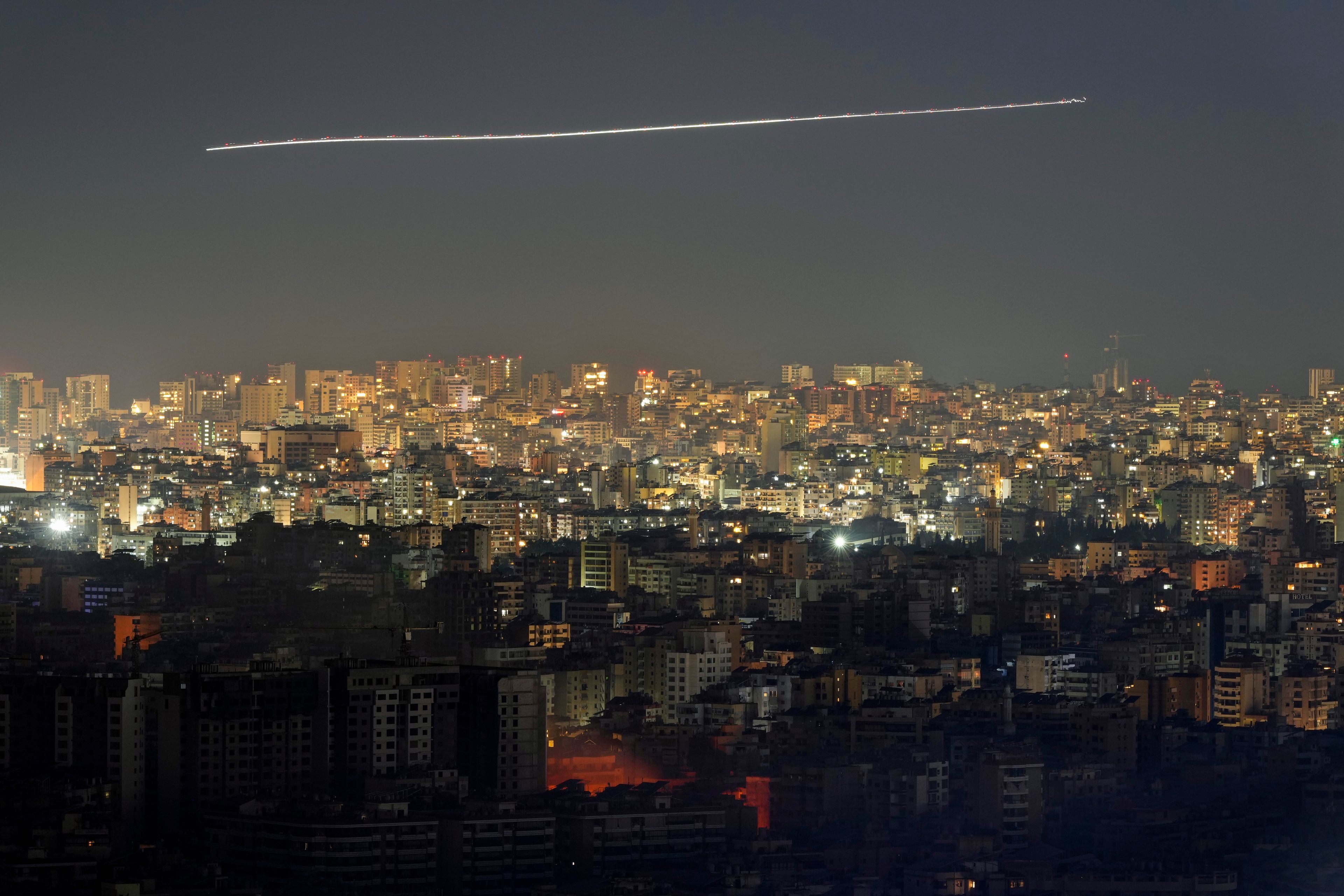 In this photo taken with slow shutter speed, a Middle East Airlines airplane flies over the capital Beirut, as fire rises from an Israeli airstrike in Dahiyeh, Lebanon, Friday, Oct. 25, 2024. (AP Photo/Hassan Ammar)