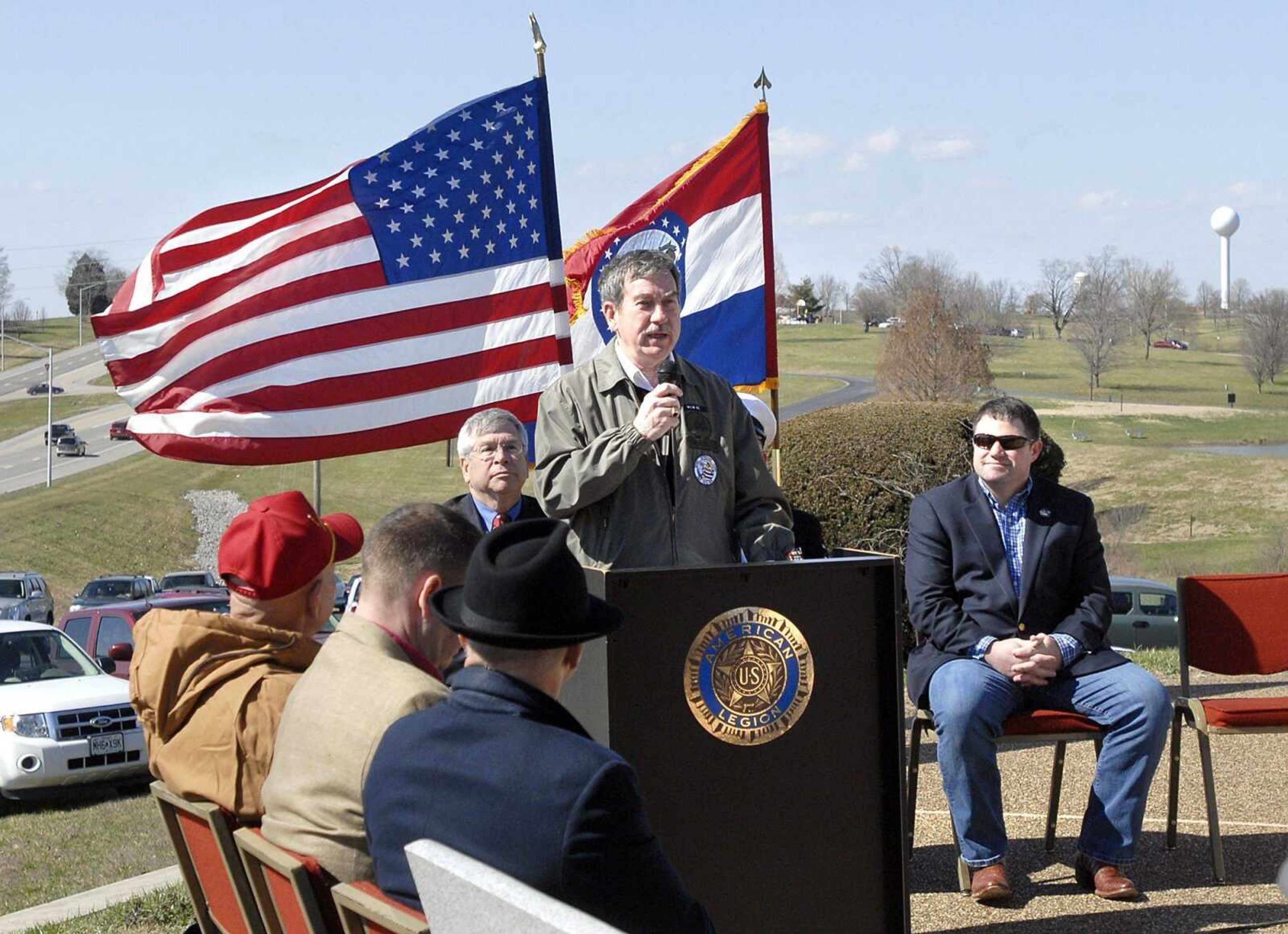 Tom Meyer tells the crowd the history of the Seabees on Saturday at Cape County Park before the dedication of a plaque commemorating the Naval unit's 70th anniversary. Seated behind Meyer are Rep. Wayne Wallingford, left, and Cape Girardeau County Presiding Commissioner Clint Tracy. Roughly 70 Seabees veterans were in attendance. (Patrick T. Sullivan)